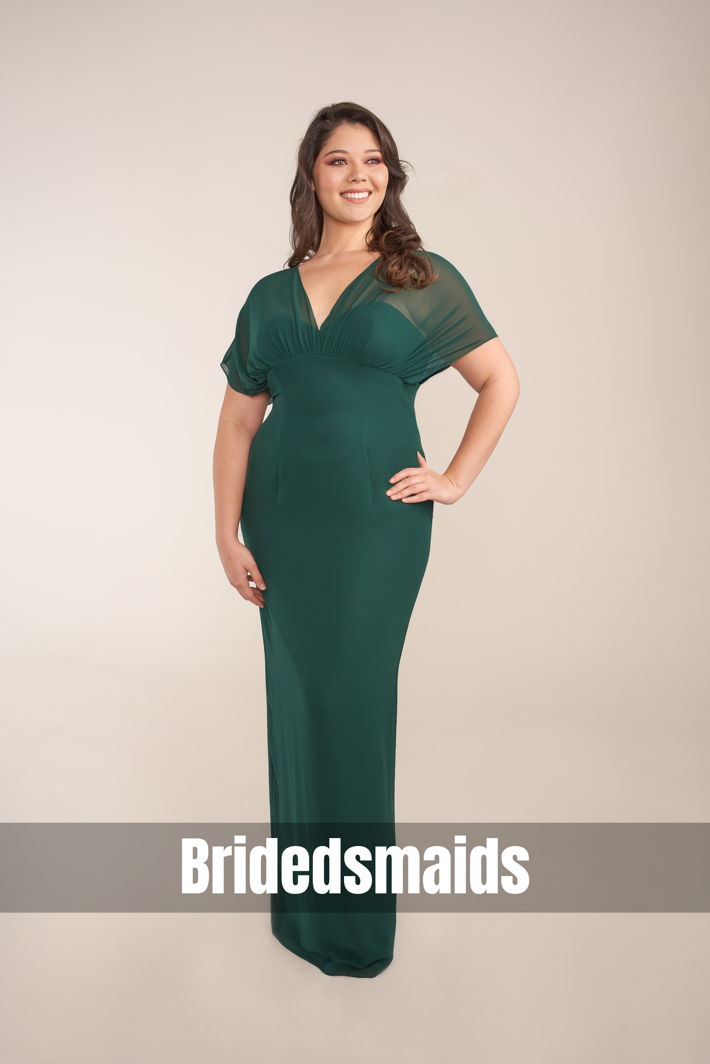 Plus-size model showcasing an emerald green bridesmaid gown with a flattering V-neckline, sheer flutter sleeves, and a sleek floor-length silhouette, styled for weddings and formal occasions.