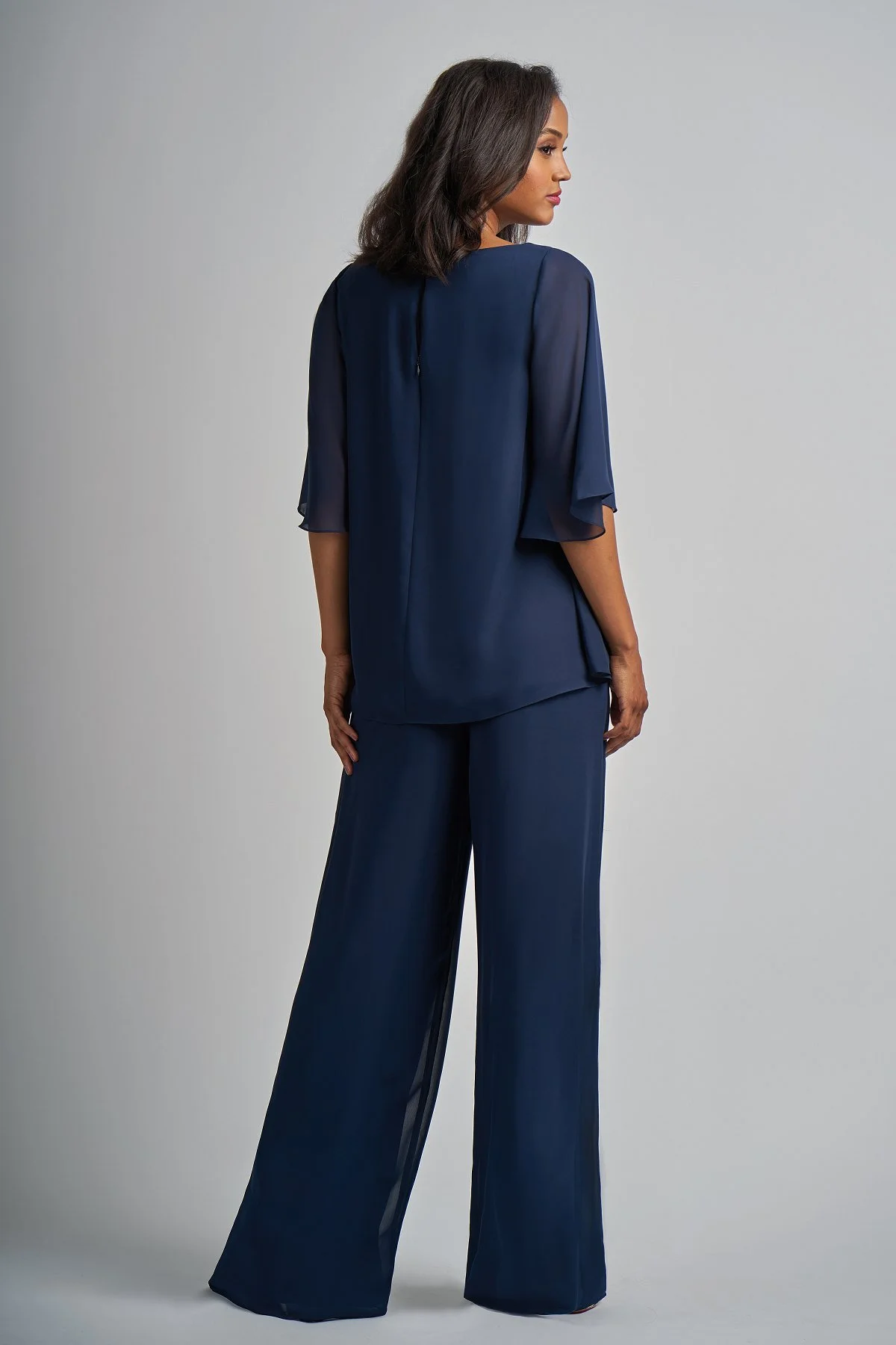 Back view of a navy mother of the bride trouser suit featuring wide-leg chiffon trousers, a flowing overlay top, and elegant flutter sleeves designed for special occasion wear.