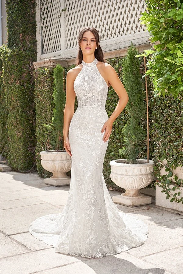 Bride models a fitted lace halter mermaid wedding dress with a high neckline, floral lace appliqués, and a graceful train in a refined garden estate, showcasing modern elegance and timeless bridal style.