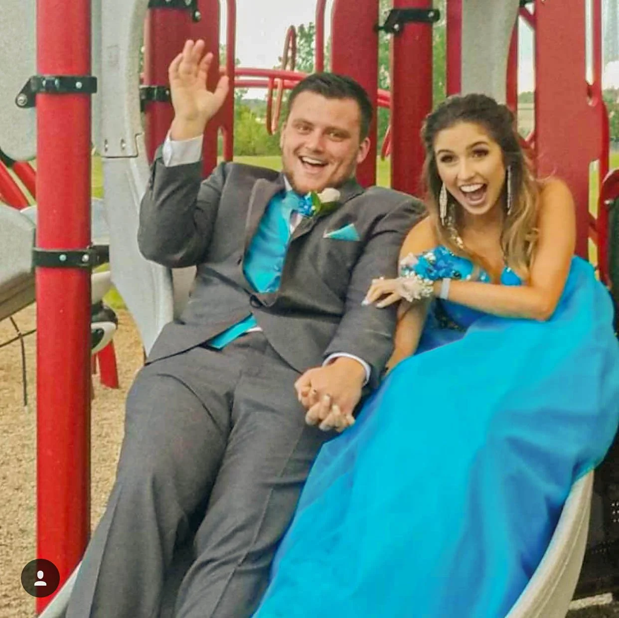 Prom couple shares a playful moment on a playground slide, showcasing coordinated turquoise and gray formalwear, including a flowing ball gown and matching suit accents for a fun and memorable prom portrait.