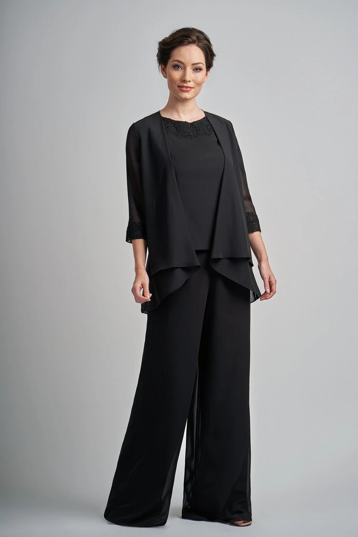 Woman modeling a black mother of the bride trouser suit featuring wide-leg chiffon trousers, a lace-trimmed sleeveless top, and an elegant waterfall-style jacket with three-quarter sleeves.