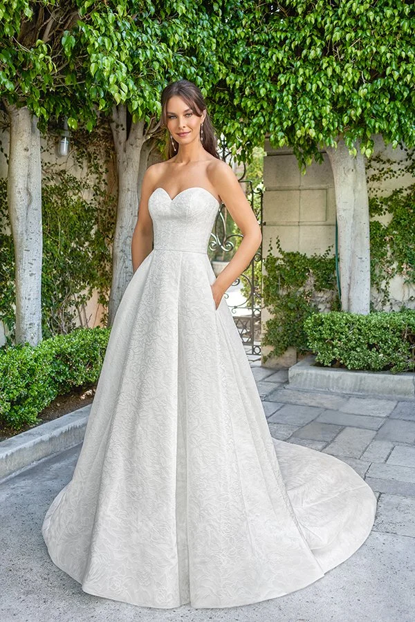Bride wearing a strapless jacquard ball gown wedding dress with a sweetheart neckline, hidden pockets, and a full cathedral train, showcasing timeless elegance in a romantic garden setting.