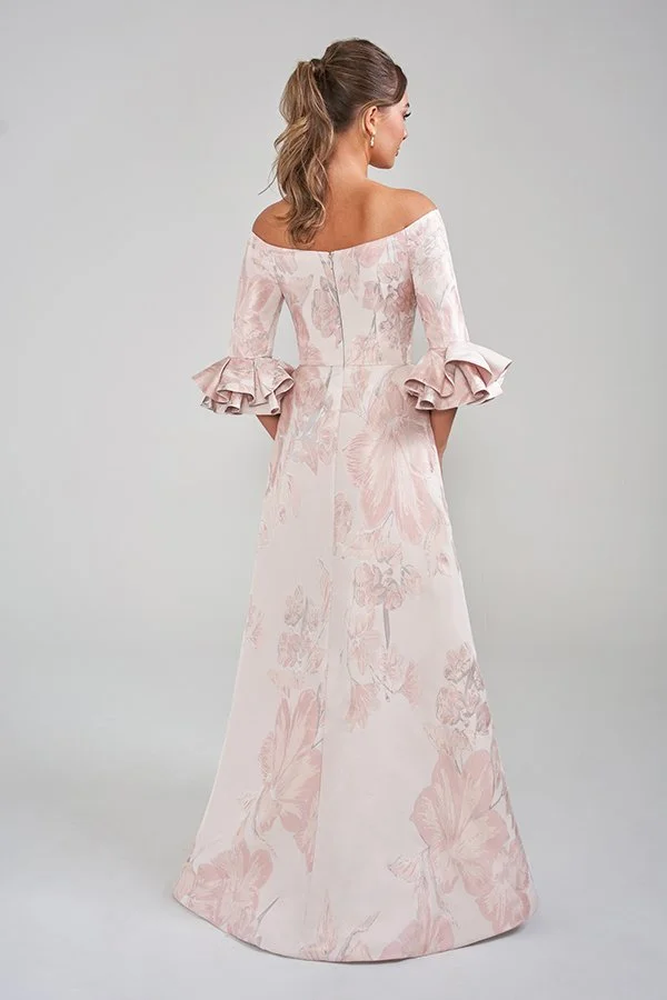Back view of an elegant blush mother of the bride gown featuring an off-the-shoulder neckline, soft floral print fabric, statement ruffle sleeve cuffs, and a graceful floor-length A-line silhouette for formal occasions.