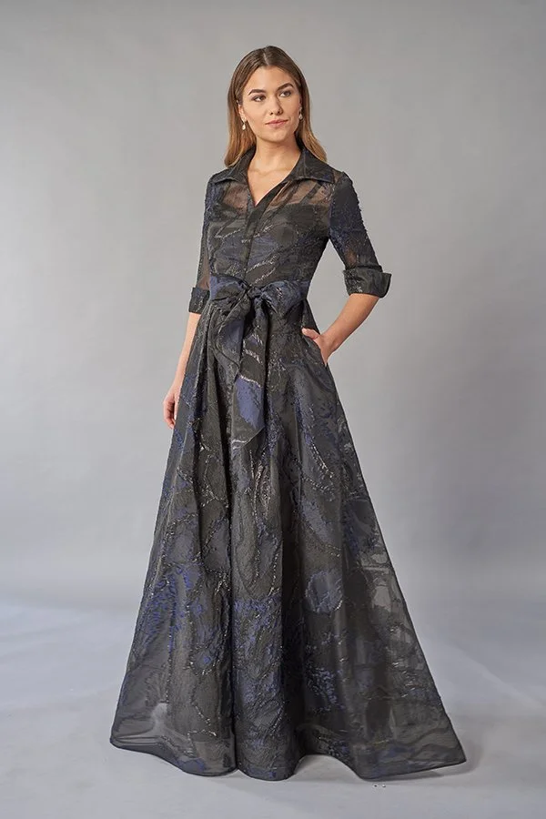 Front view of an elegant charcoal mother of the bride gown with a collared neckline, sheer three-quarter sleeves, metallic cobalt jacquard fabric, waist tie belt, and flowing A-line skirt with pockets.