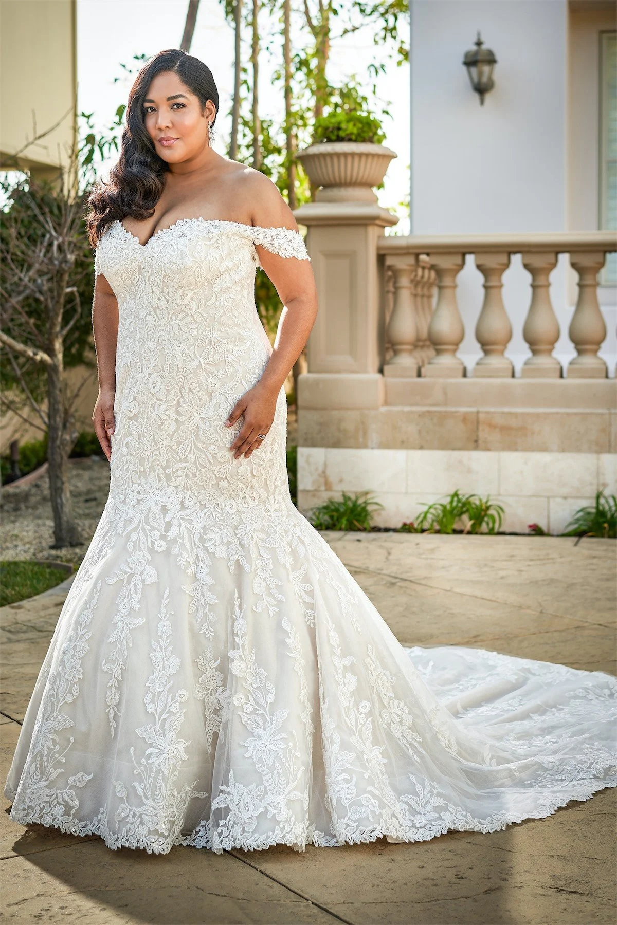 Bride models a plus-size off-the-shoulder lace mermaid wedding dress with a sweetheart neckline and flowing train, showcasing elegant bridal fashion, flattering curves, and timeless outdoor wedding inspiration.