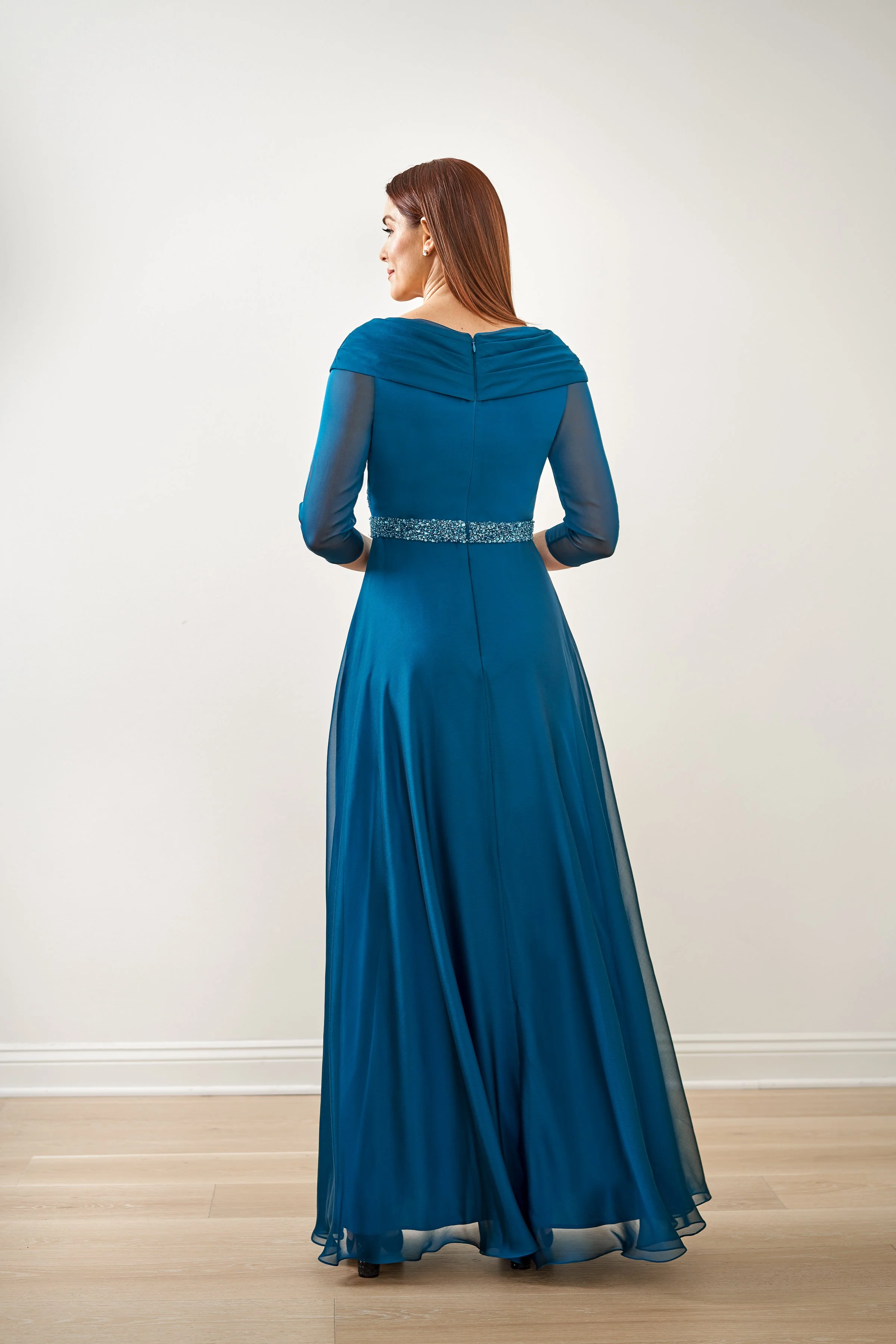Back view of a teal mother of the bride gown with an off-the-shoulder neckline, sheer three-quarter sleeves, crystal beaded waistband, and a flowing chiffon A-line skirt for formal occasions.