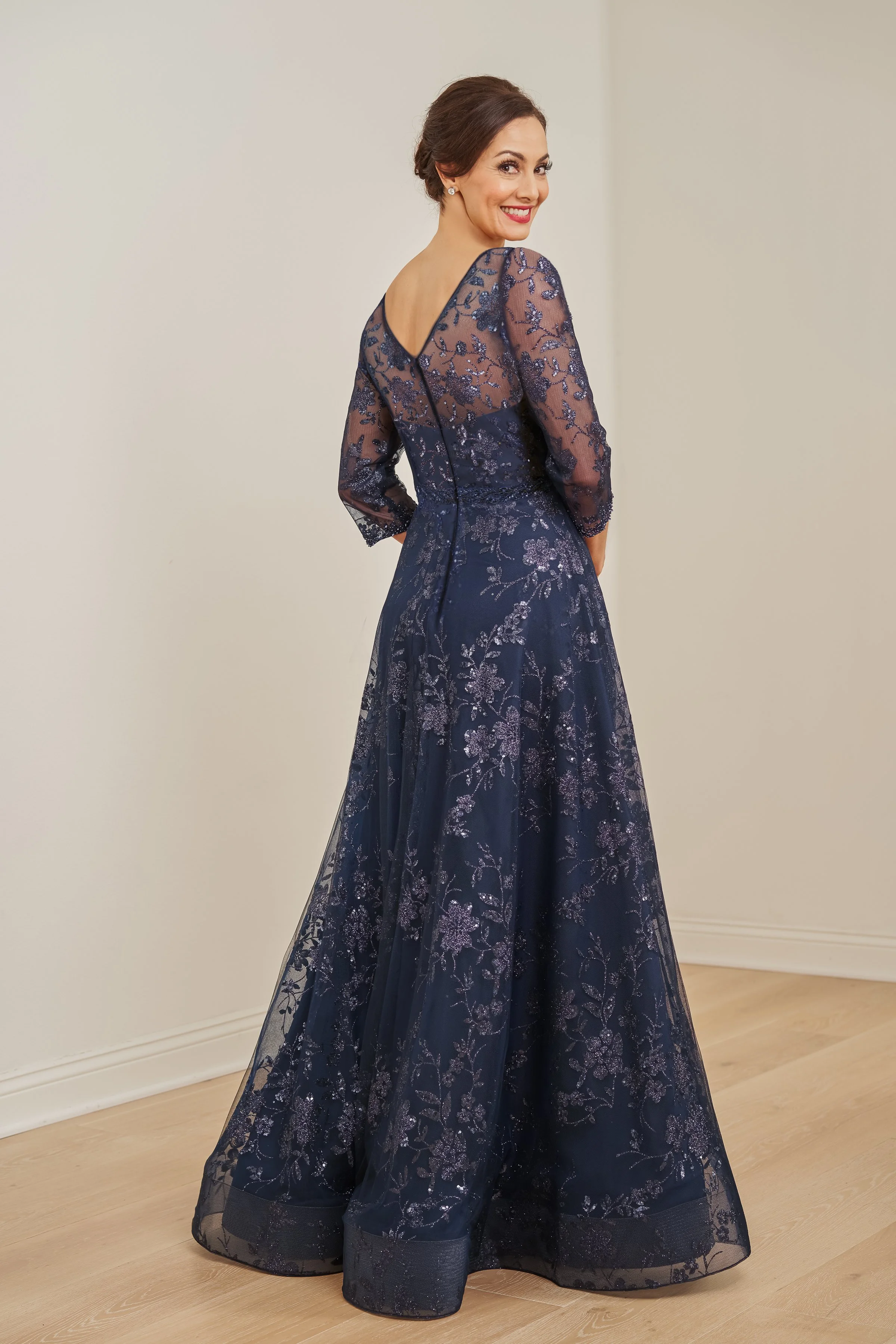 Back view of a navy mother of the bride gown with a V-back illusion neckline, sheer three-quarter sleeves, glitter floral embroidery, and a flowing A-line silhouette ideal for weddings and formal occasions.