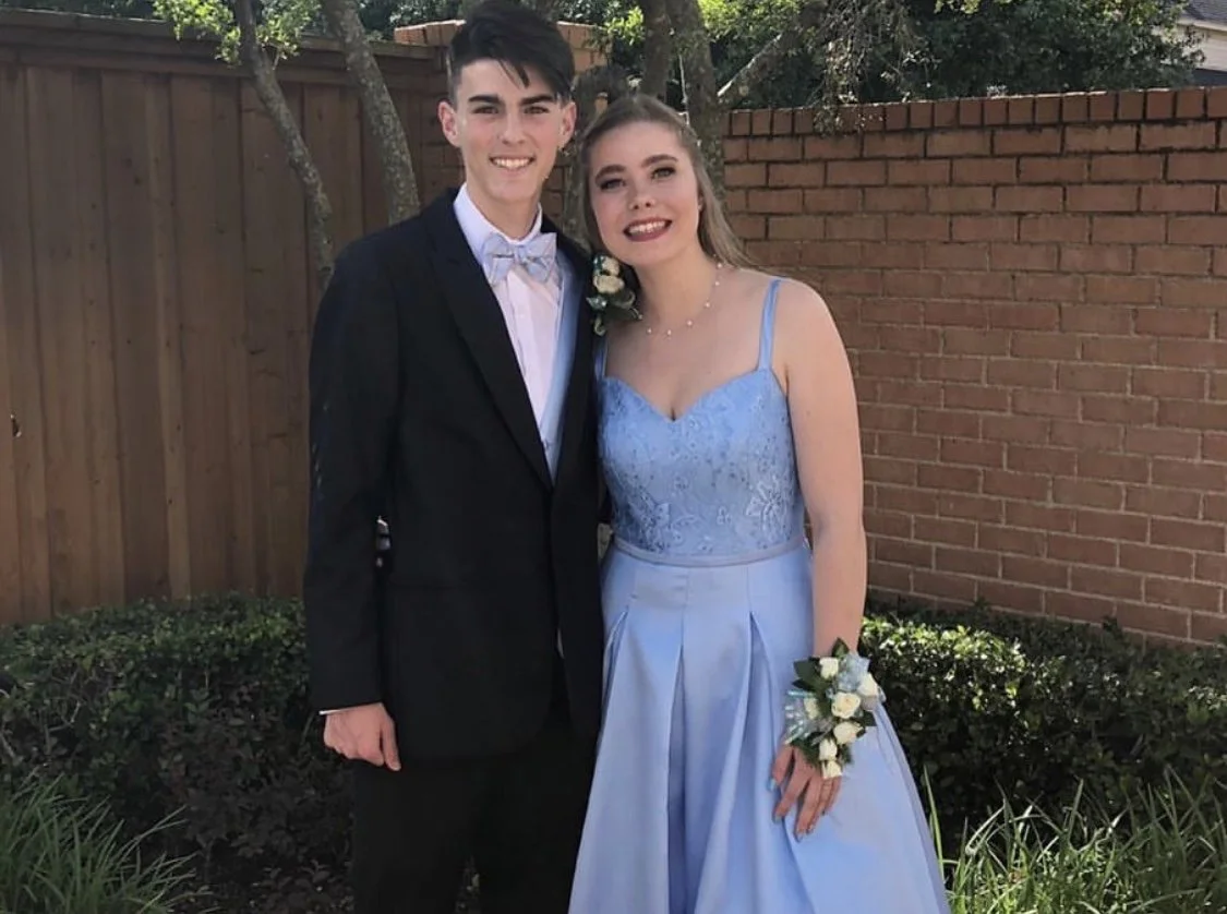 Prom couple smiling together in coordinated formalwear, featuring a light blue gown with a lace bodice and flowing skirt paired with a classic black suit and bow tie, creating a timeless outdoor prom portrait.