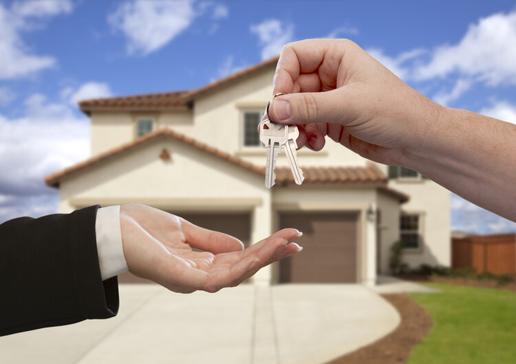 Person handing over house keys in front of a residential home.