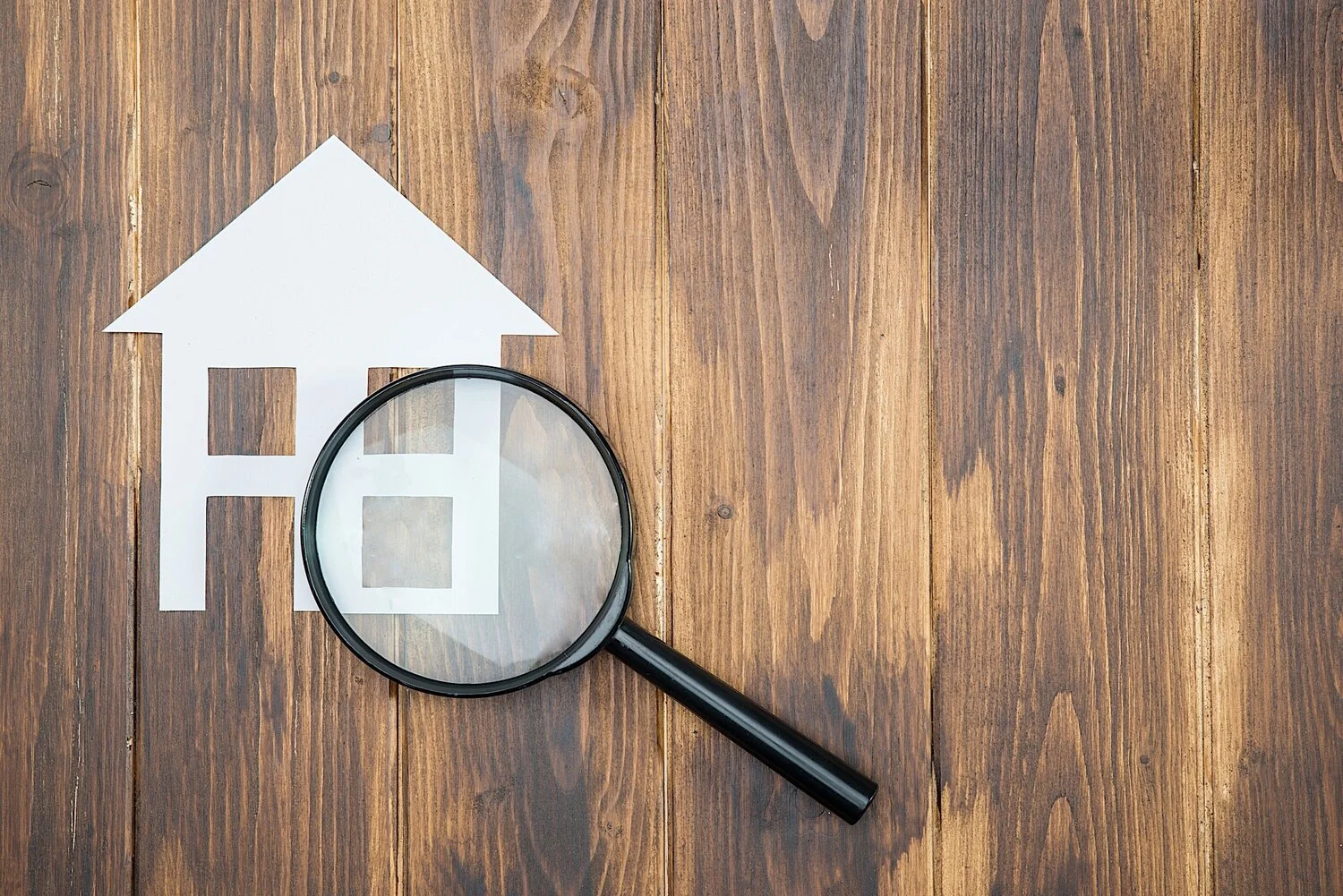 Magnifying glass over a house icon representing a new homeowner property checklist.