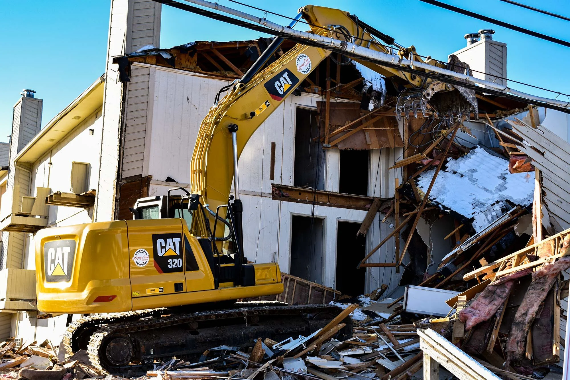 Excavator demolishing a residential building with debris around the jobsite.