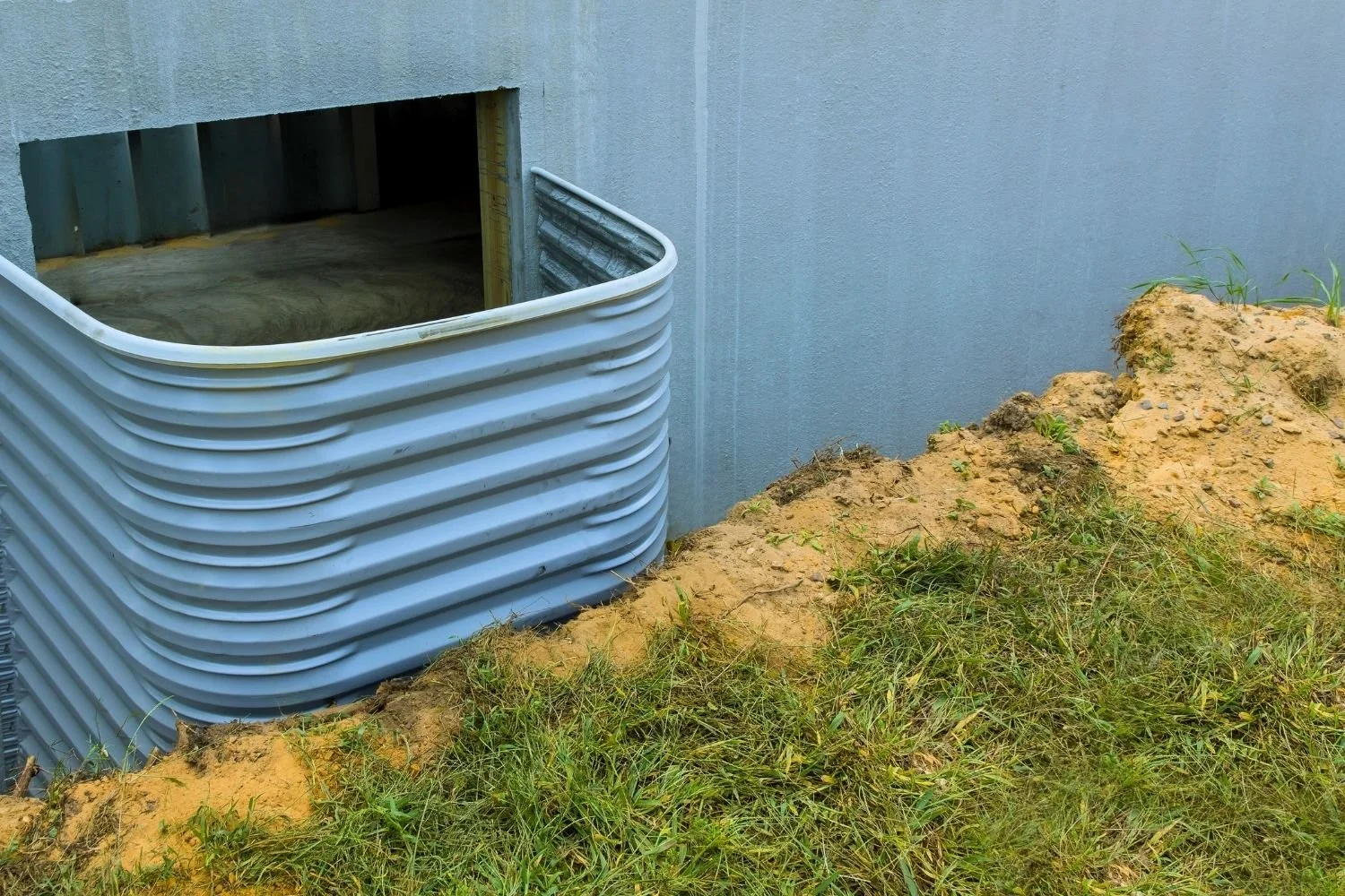 Graded soil sloping near a basement window well on a residential property.