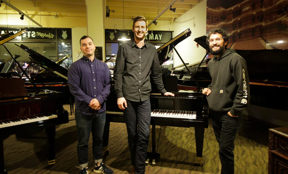 A photo of three members of the seattle piano moving team in front of a black bosendorfer grand piano and surrounded by several other grand pianos in a showroom