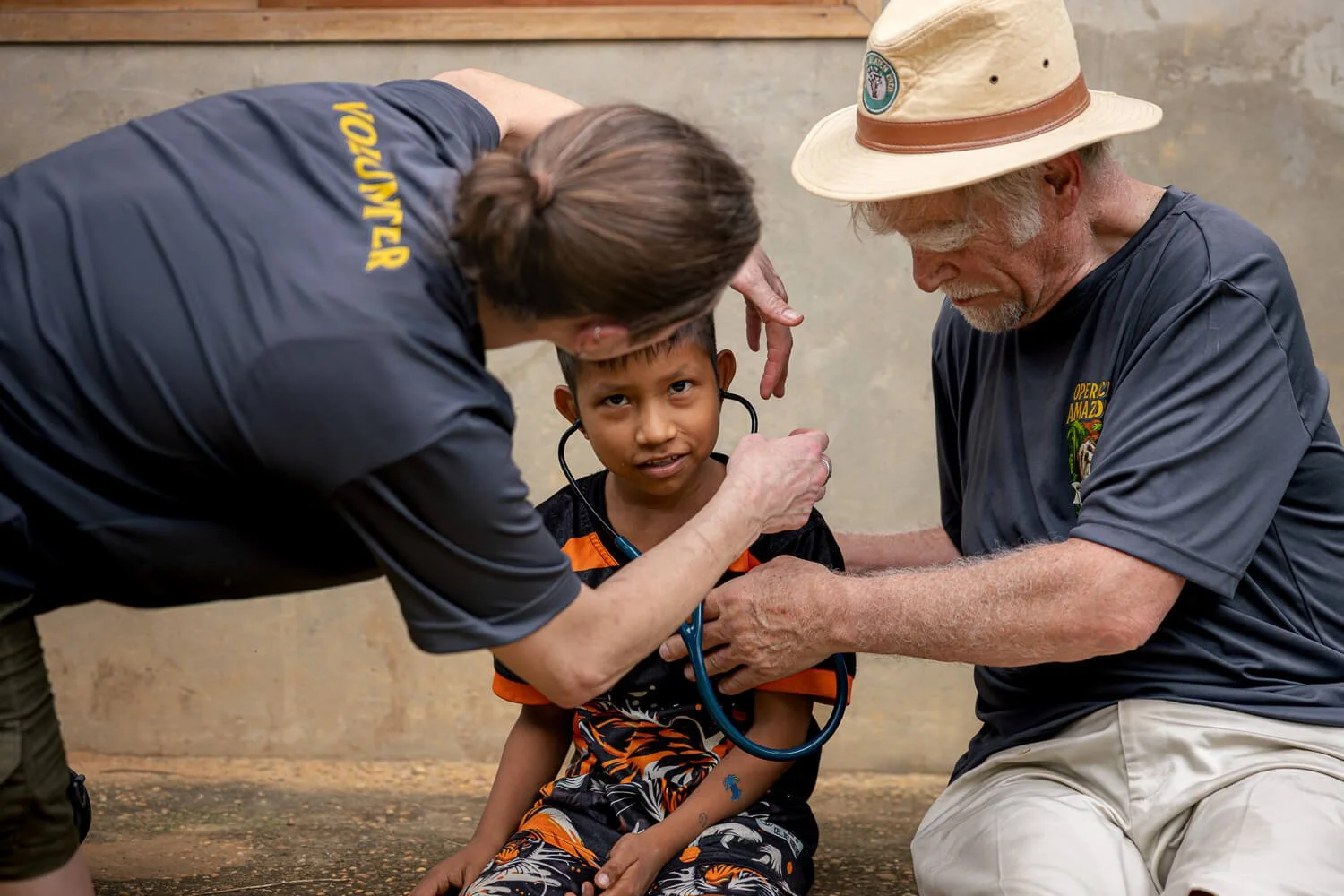 A member of the veterinary team holds a stethoscope to a smiling boy’s ears while the veterinarian looks on.