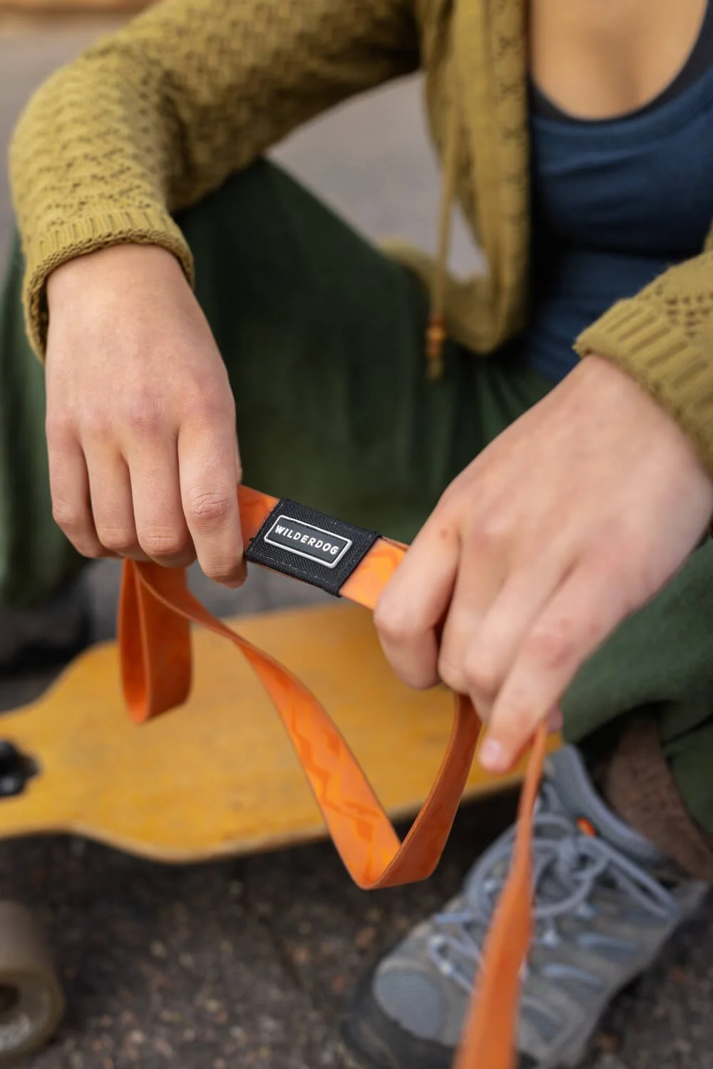 Close-up of a person's hands holding an orange woven dog leash with the black Wilderdog brand tag visible.