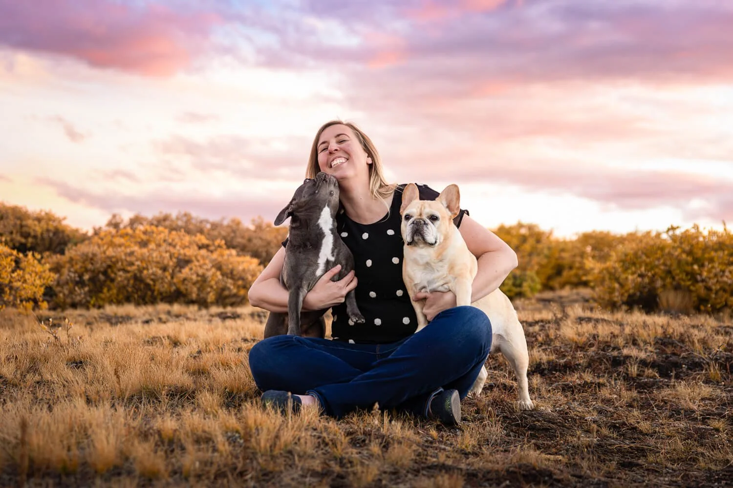 A joyful portrait of a woman embracing her French Bulldog against a pastel sunset sky, specialized dog photography in Boulder, Colorado.