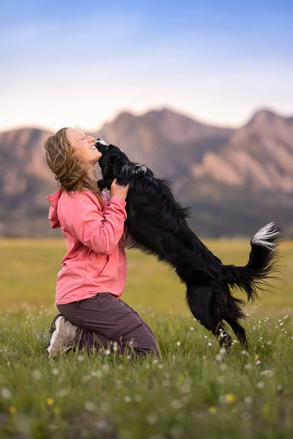 Happy black and white border collie gives dog trainer, Jenn Fantasia, kisses while on a hike in Boulder.