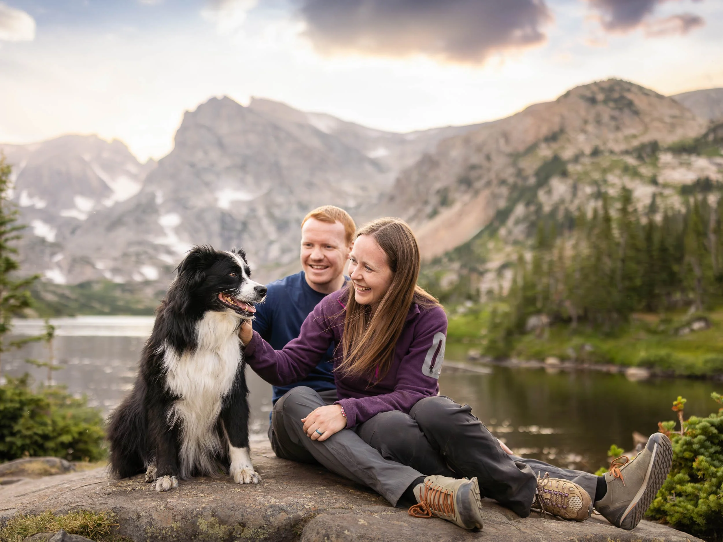 Portrait of a happy couple with their dog in front of an alpine lake during a dog photography session in the mountains.