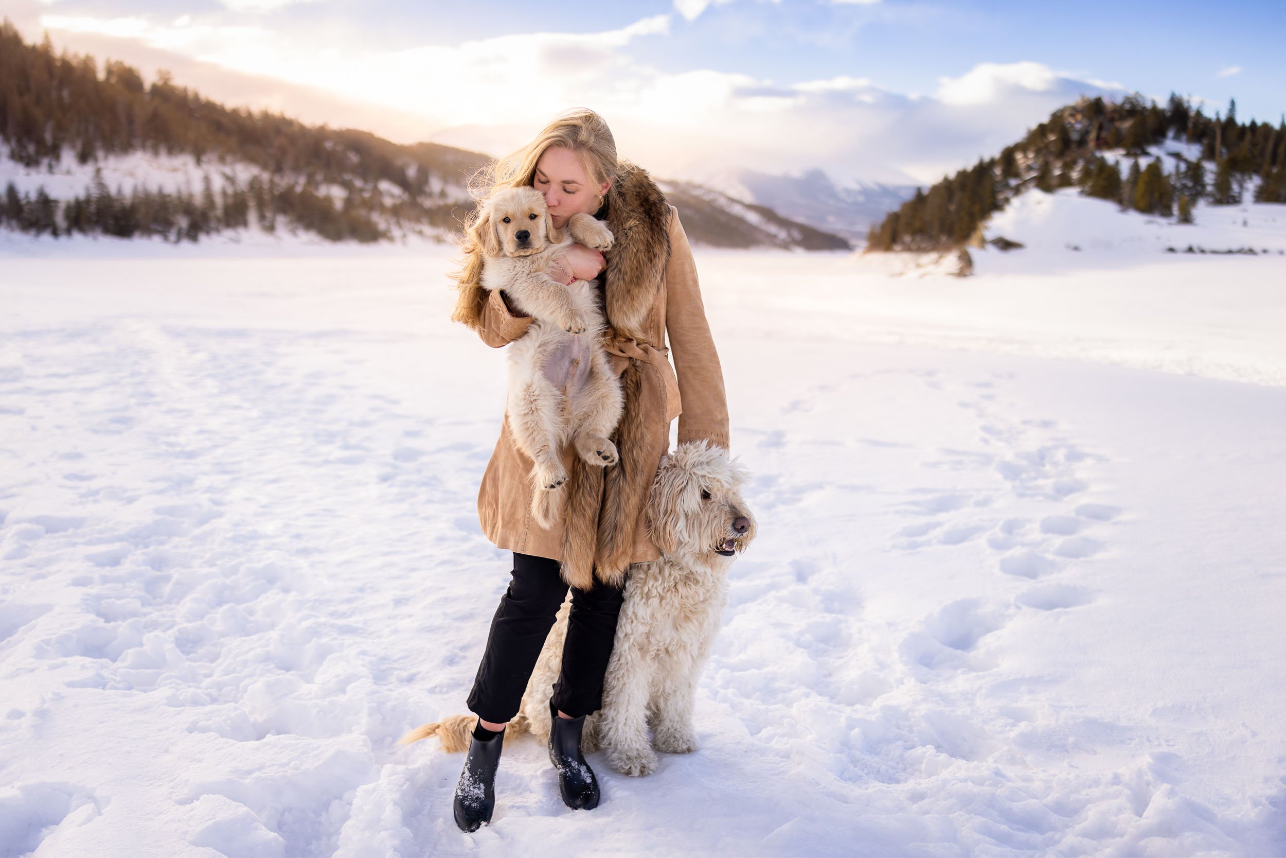 Woman snuggling with Golden Retriever and adult doodle during a winter dog photography shoot near Denver, Colorado.