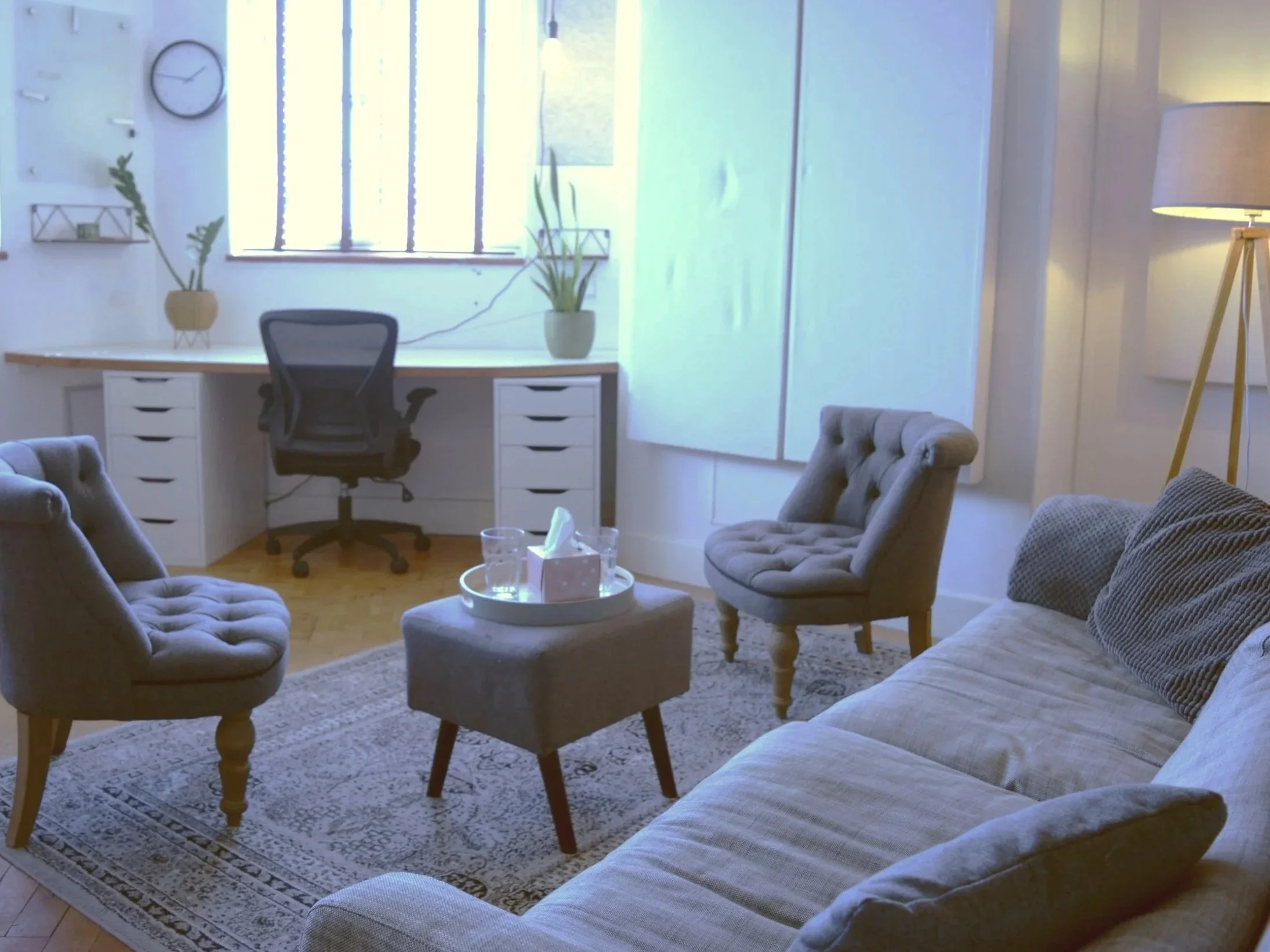A calming counselling space in Lewes with a sofa and two chairs.  Natural light comes in through the window and a standing lamp provides a warm glow.