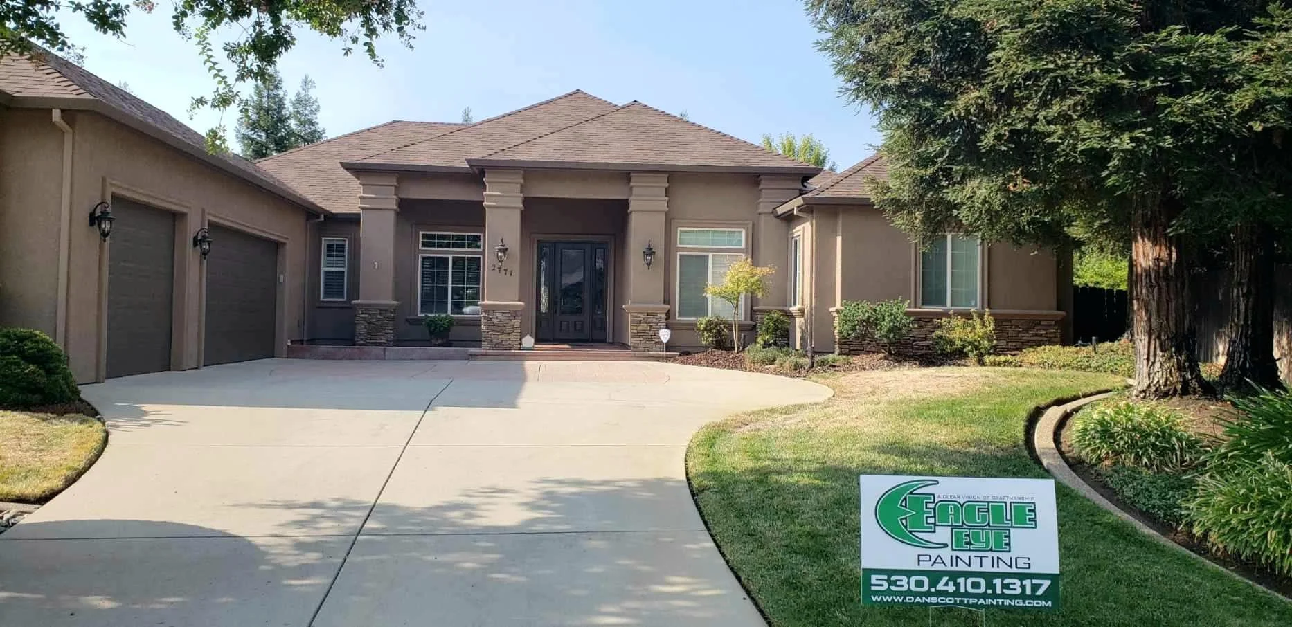 Front view of a modern house with two garage doors, a paved driveway, and a sign in the yard advertising Eagle Eye Painting with a phone number and website.