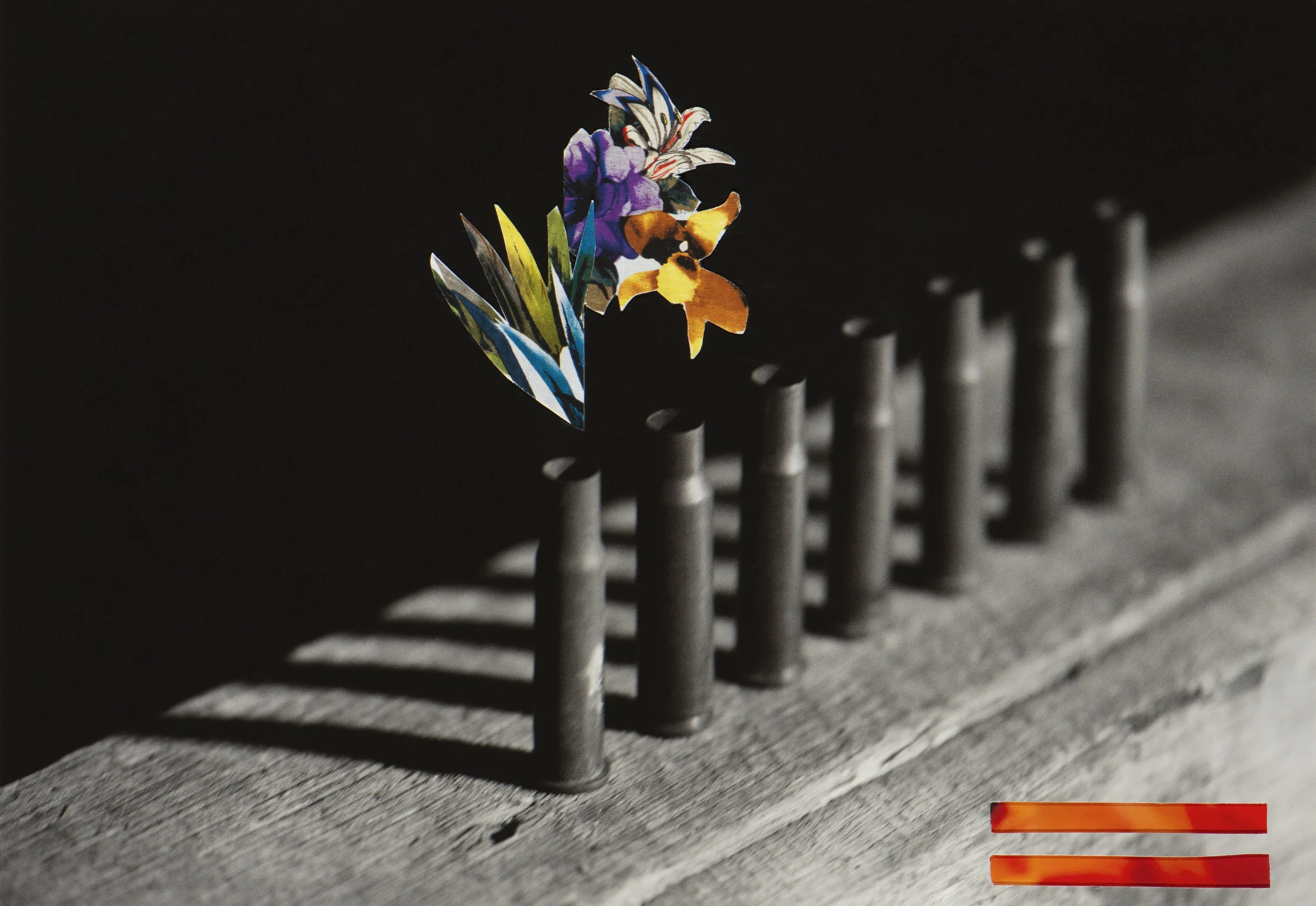 A small paper collage of colorful flowers and a butterfly placed on the head of a metal security grill on a weathered wooden surface, with a blurred background
