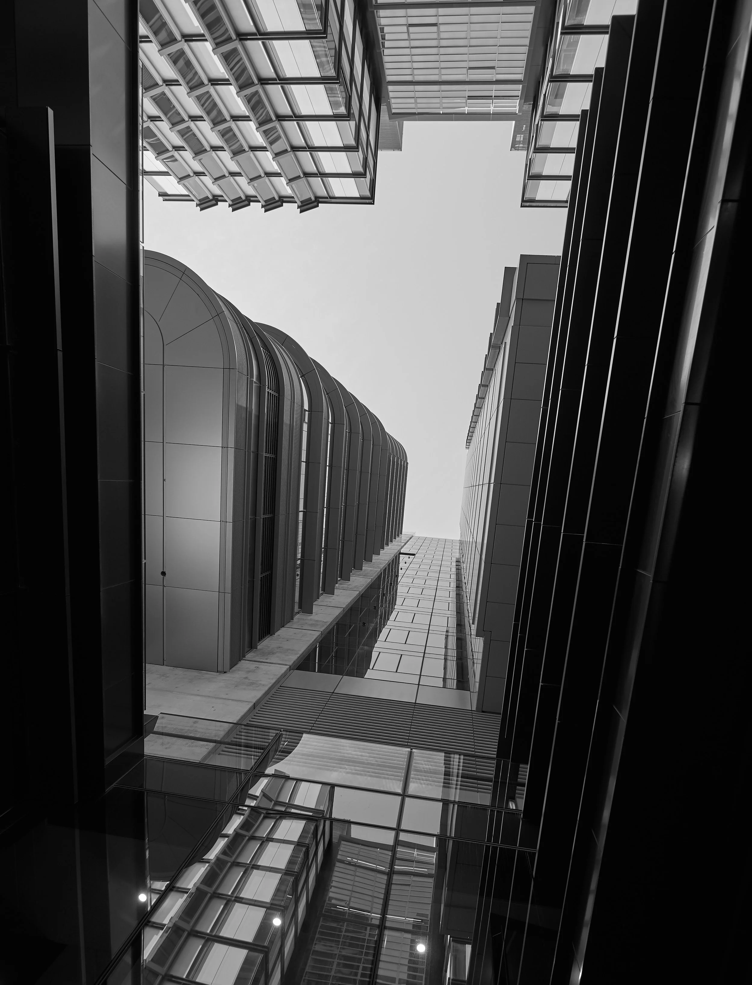 Looking up at tall, modern skyscrapers in a city, with a view from the ground through an open courtyard at the sky.