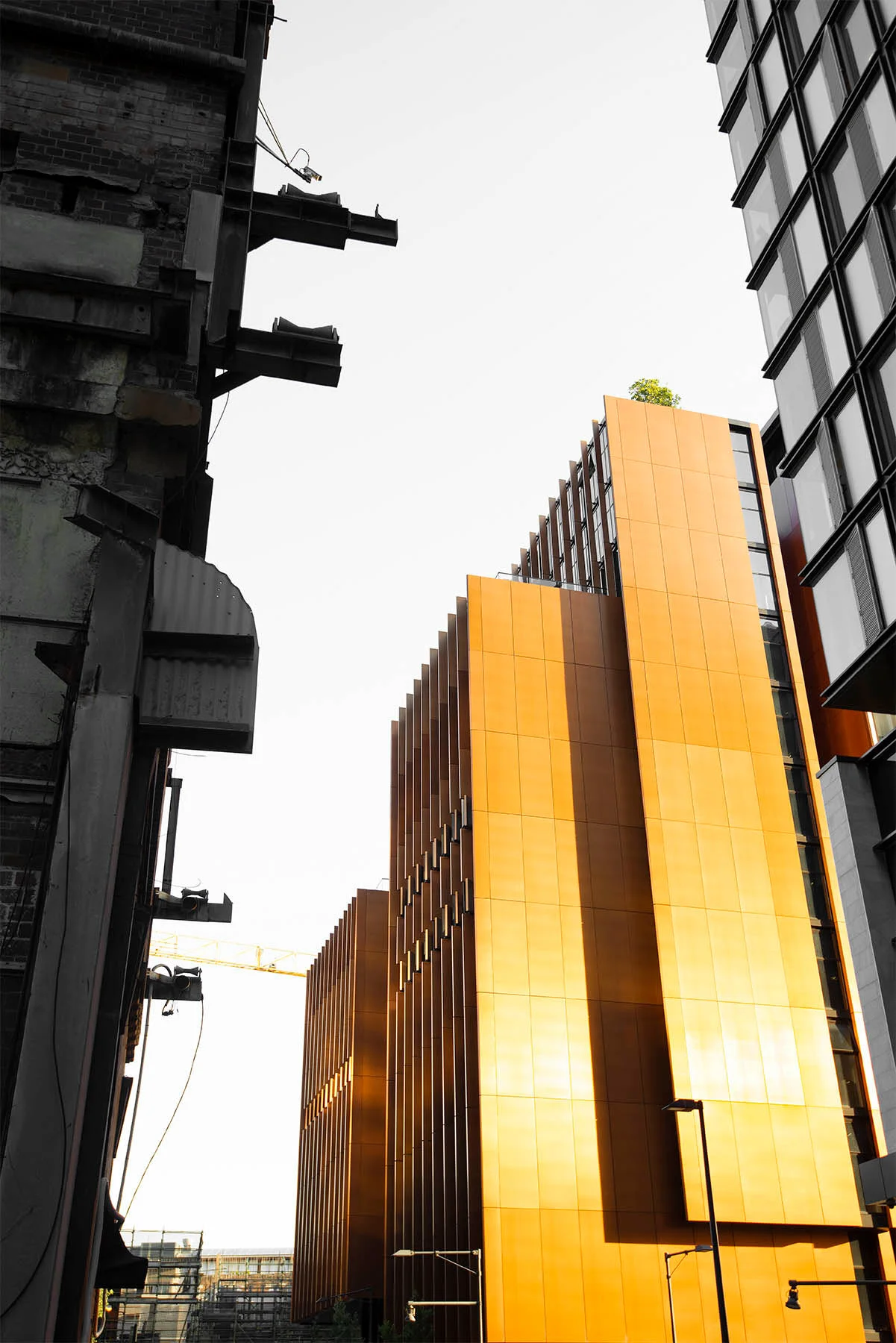 Tall modern building with reflective orange panels in an urban setting, contrasting with an older dark building on the left.