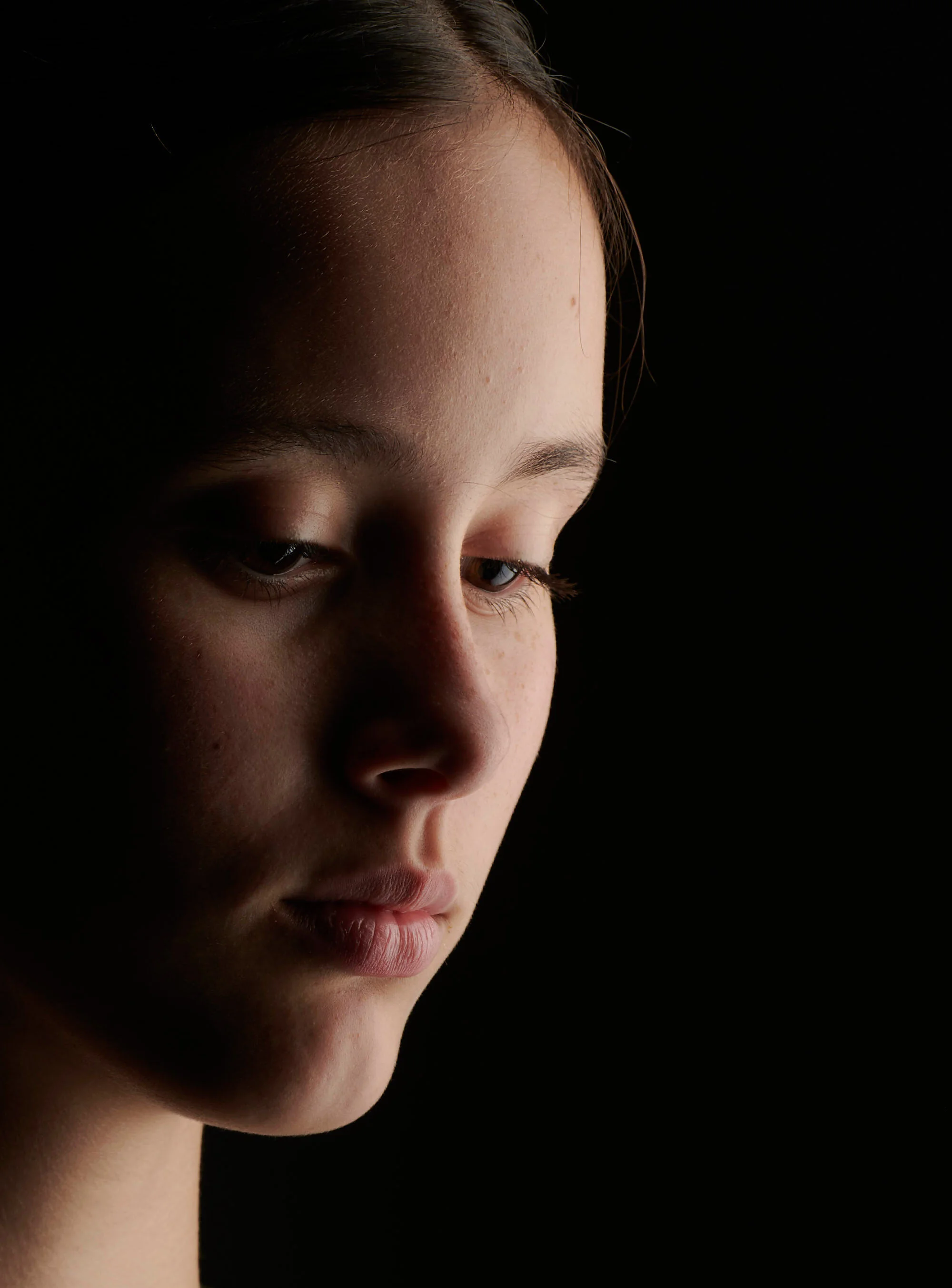 Close-up of a young woman's face with light illuminating her features against a dark background.