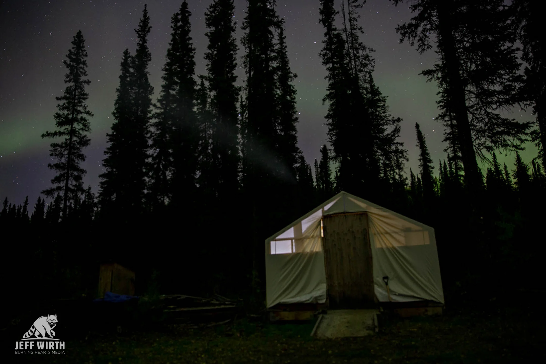 The northern lights (aurora borealis) dance overhead a wall tent at the wildlife blockade in the Sacred Headwaters. Sacred Headwaters, BC, Canada.
