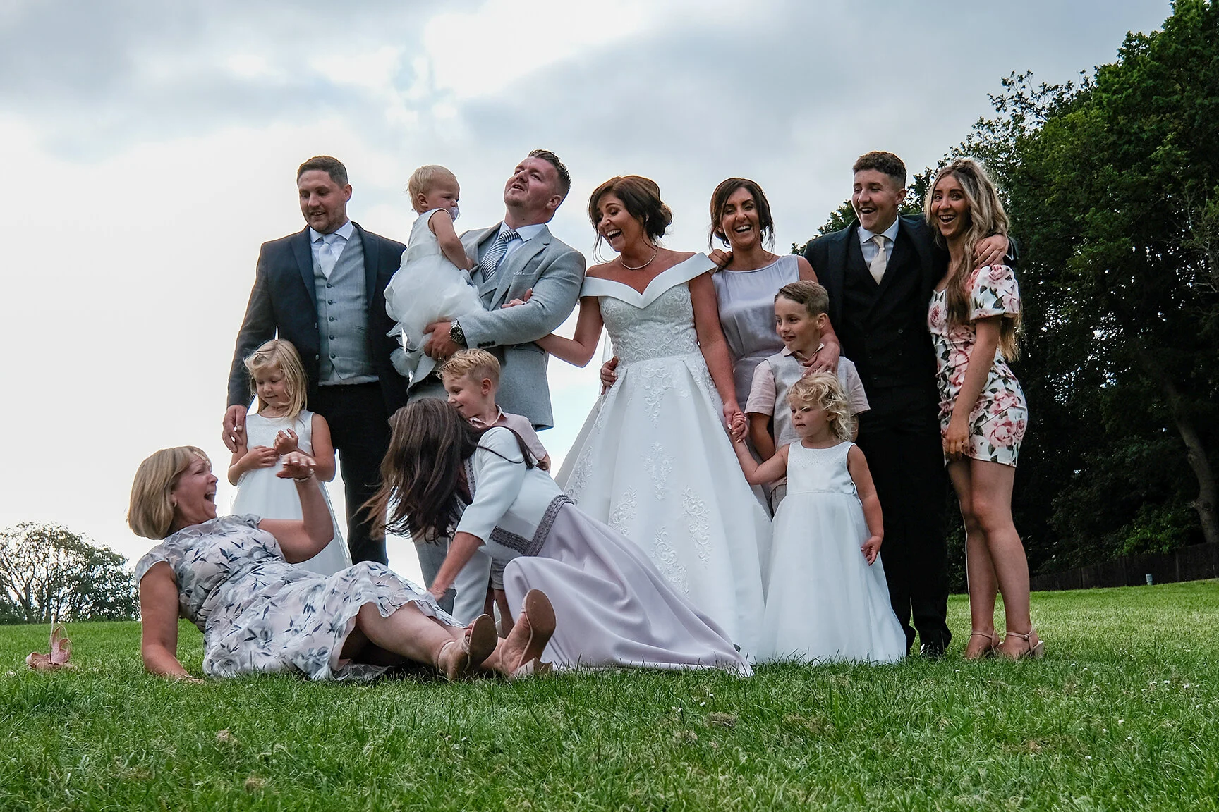Group photo at a wedding with one guest pictured on the floor after slipping captured in a candid documentary photography style
