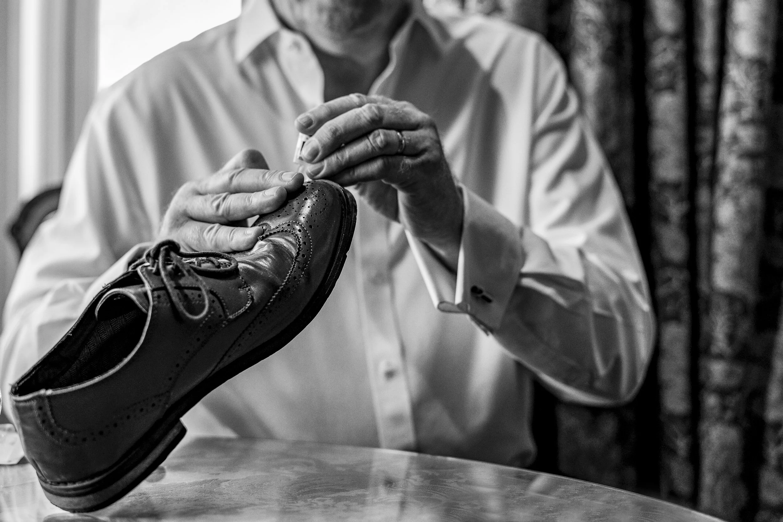 Father of the bride repairing a shoe before the ceremony captured in a candid moment by a documentary wedding photographer