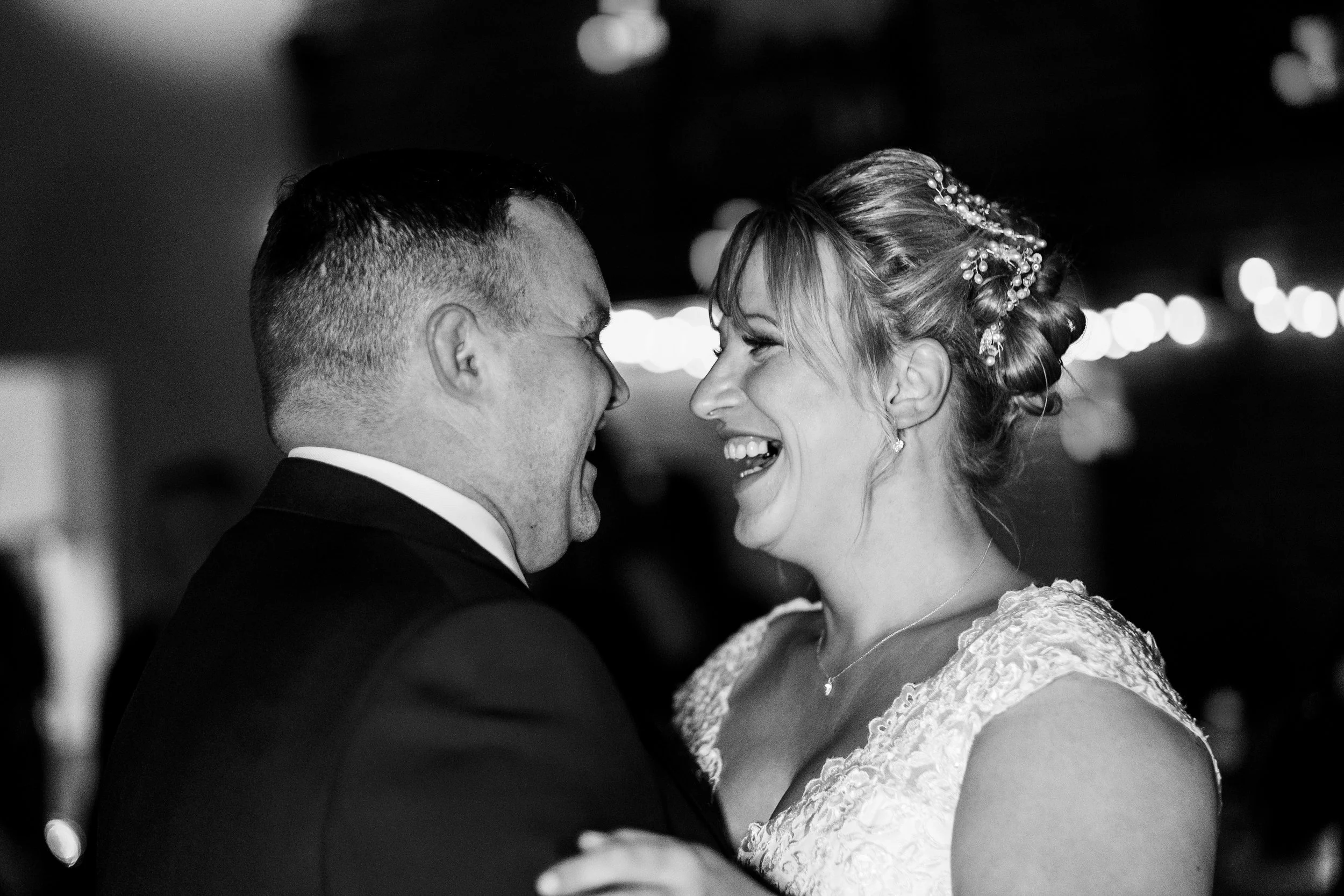 A black and white photo of a smiling couple on their wedding day, close together with faces touching, in a joyful embrace.