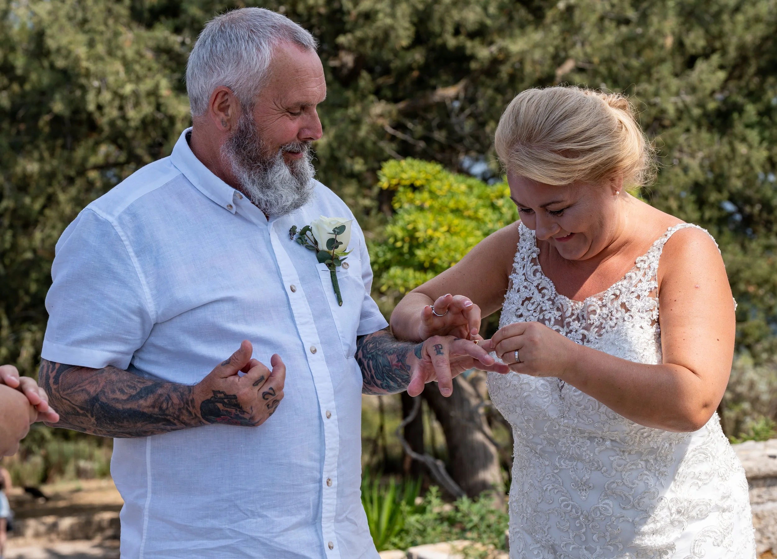 A couple participating in a wedding ceremony outdoors, with the man placing a ring on the woman's finger.