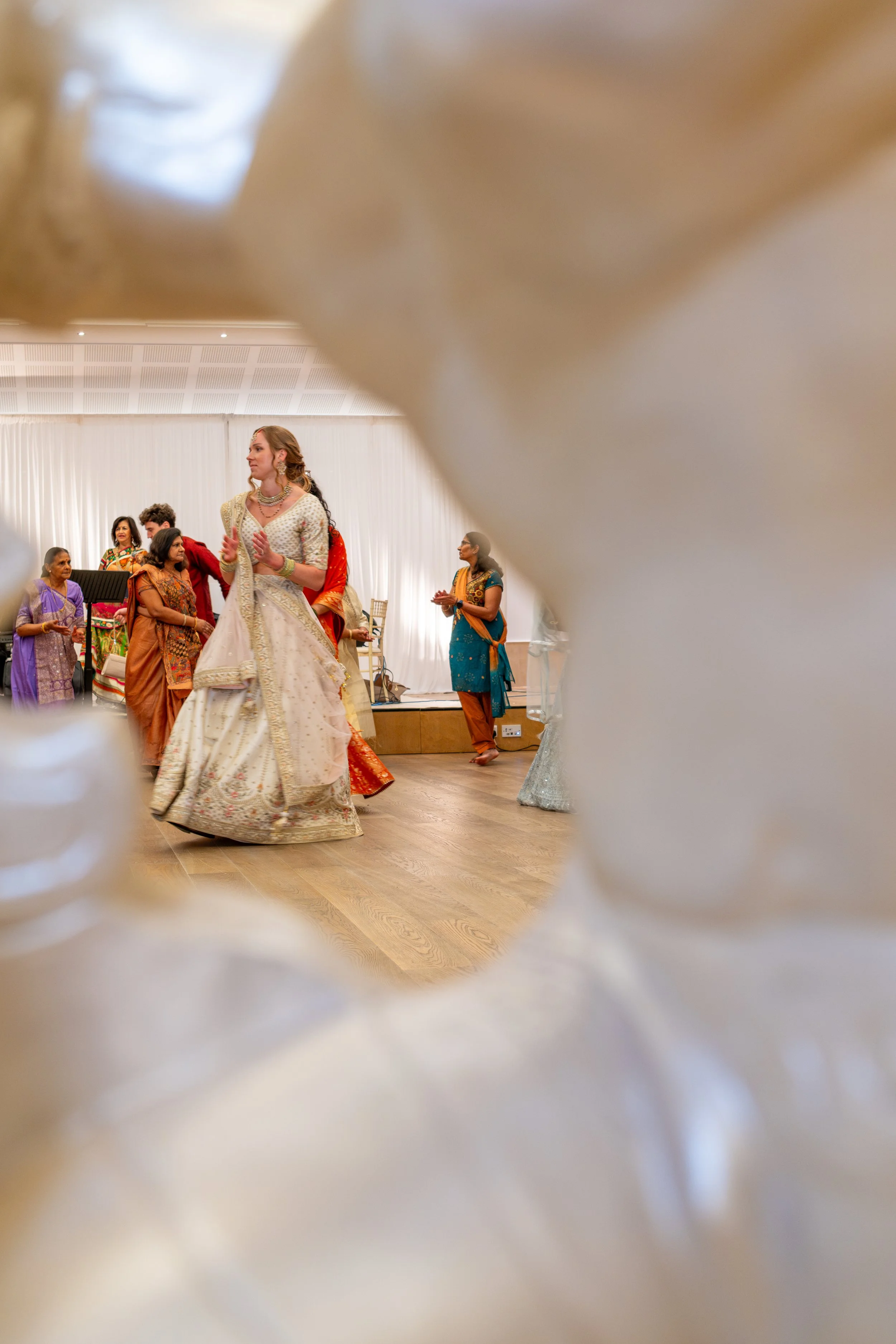 People dressed in traditional Indian attire dancing at a celebration or cultural event, with a white draped backdrop.