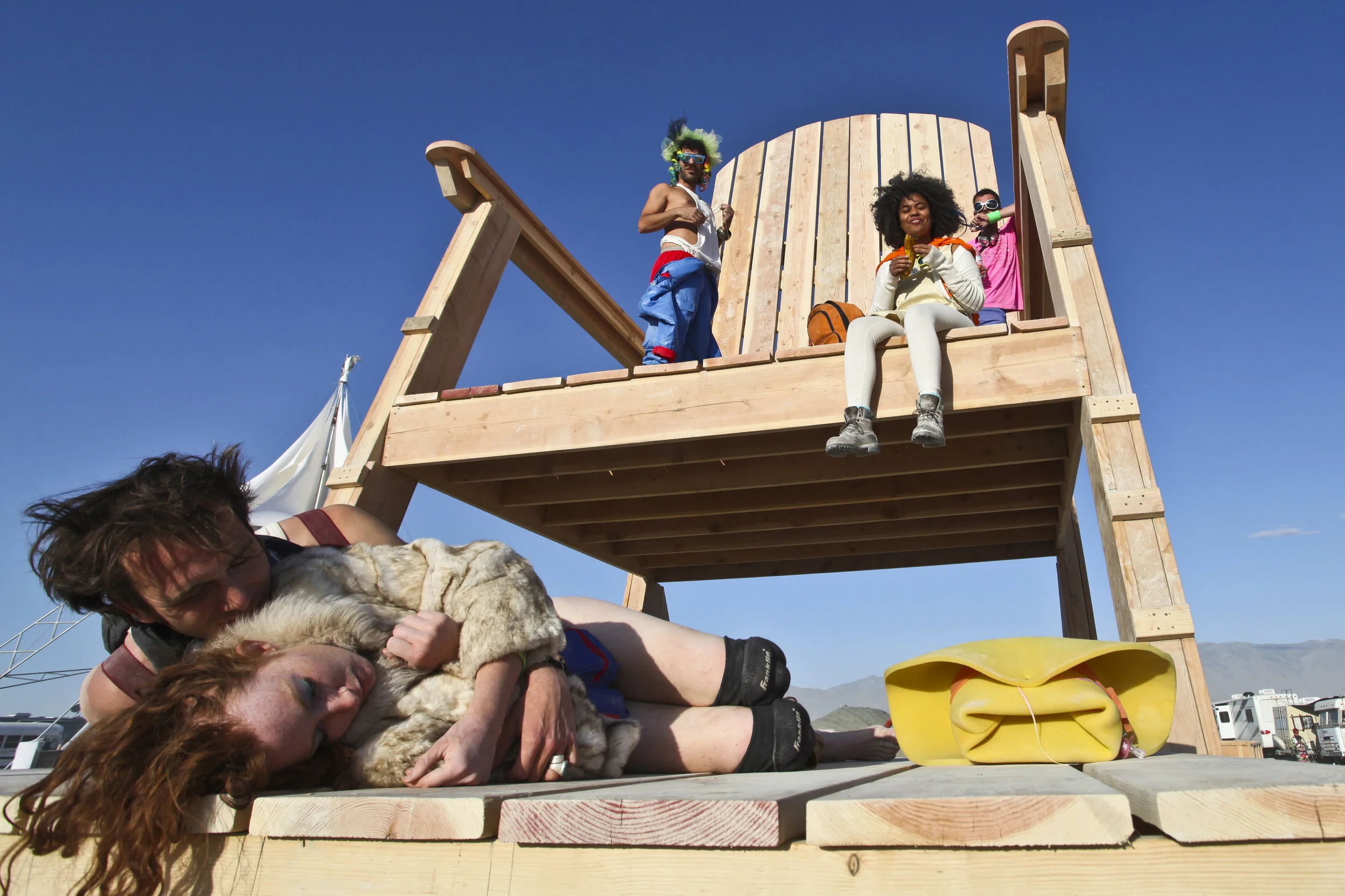  A group of people hang out on a large wooden chair that was built on the playa. The chair was also burnt at the end of the week. 