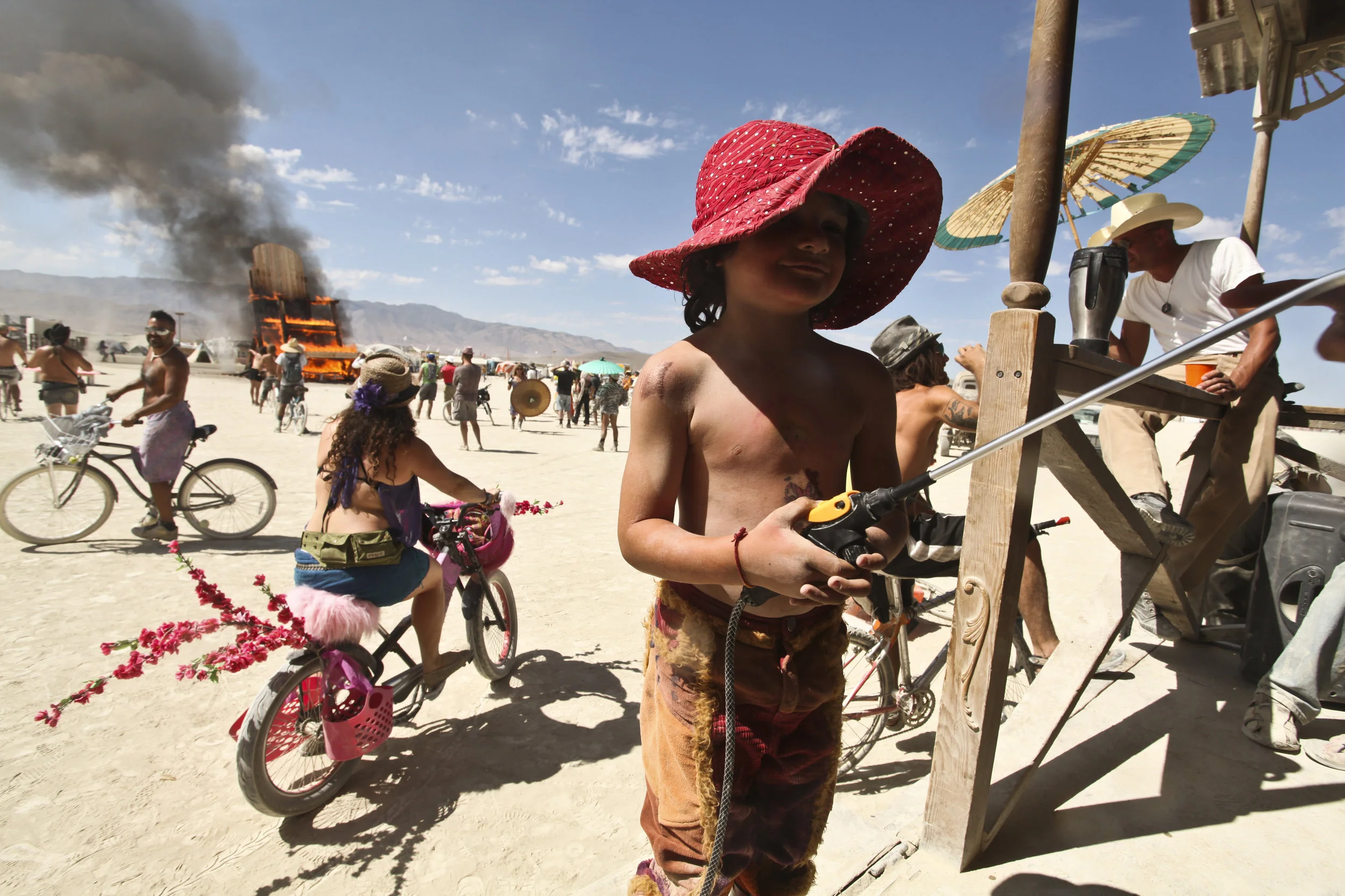  A young boy sprays a woman with a water sprayer as a giant chair burns. 