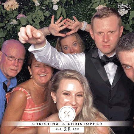 Group of five people at a wedding celebration, some making funny faces and gestures, with a backdrop of greenery. The bride and groom, Christina and Christopher, are in the front, with the wedding date August 28, 2021, displayed below.