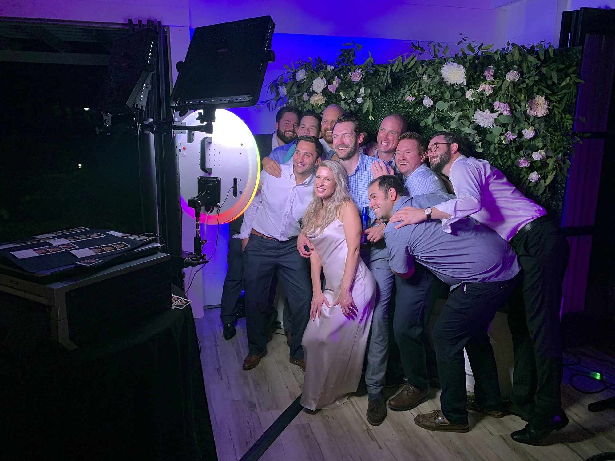 Group of people taking a photo together at a party with a camera and a floral backdrop.