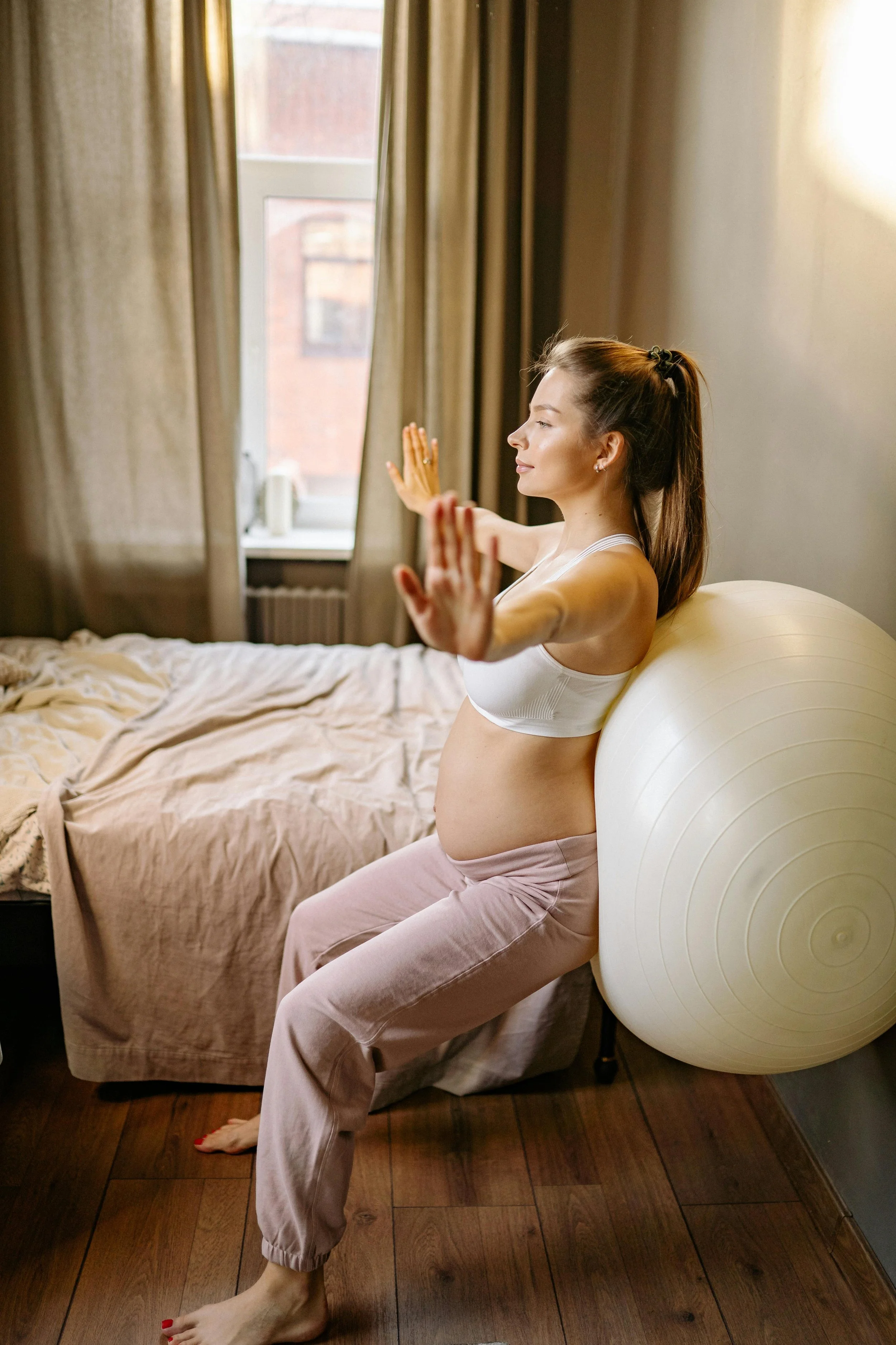 A pregnant woman sitting against a birthing ball with her hands extended in a calm breathing exercise, representing second trimester prenatal support at South Shore Acupuncture and Wellness, Rockland MA.