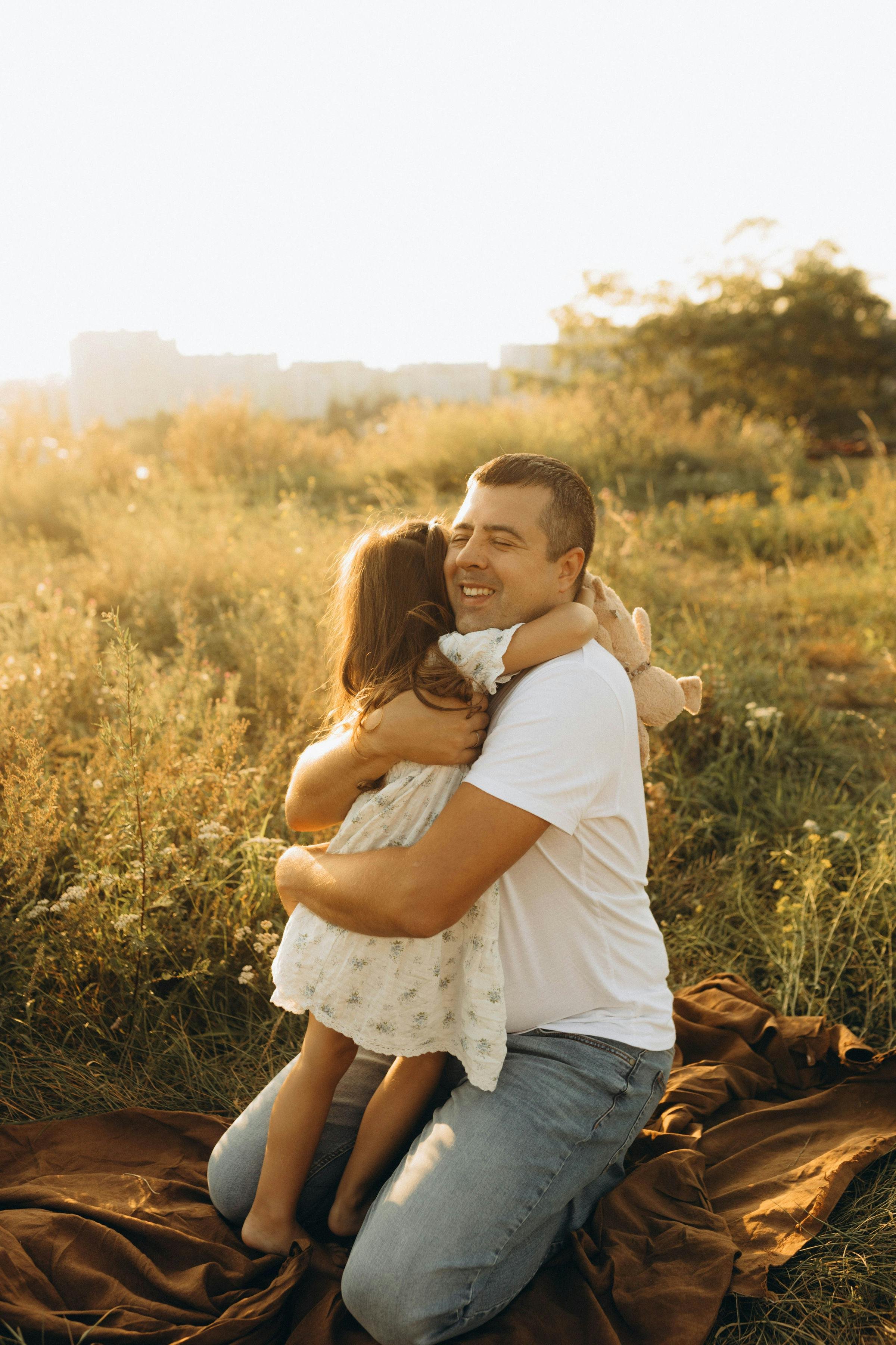 A father hugging his young daughter in a golden field at sunset, representing male factor fertility and sperm health support at South Shore Acupuncture and Wellness, Rockland MA.