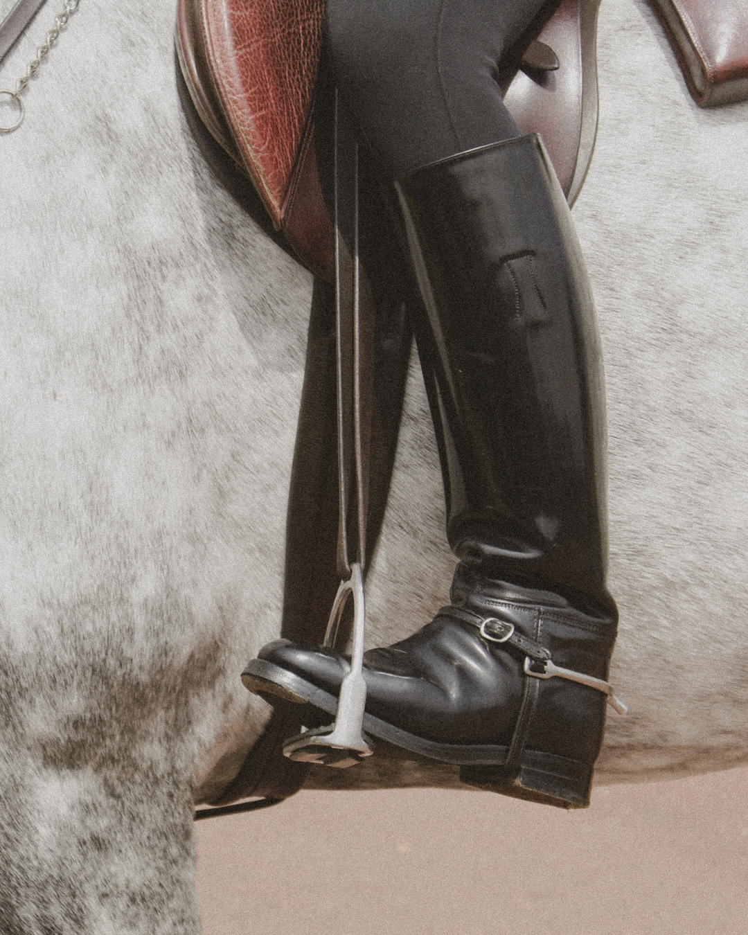 Close up photograph of a rider’s lower leg and boot resting in a stirrup against the side of a horse, emphasizing the ankle and foot bearing weight and maintaining balance during sustained activity.