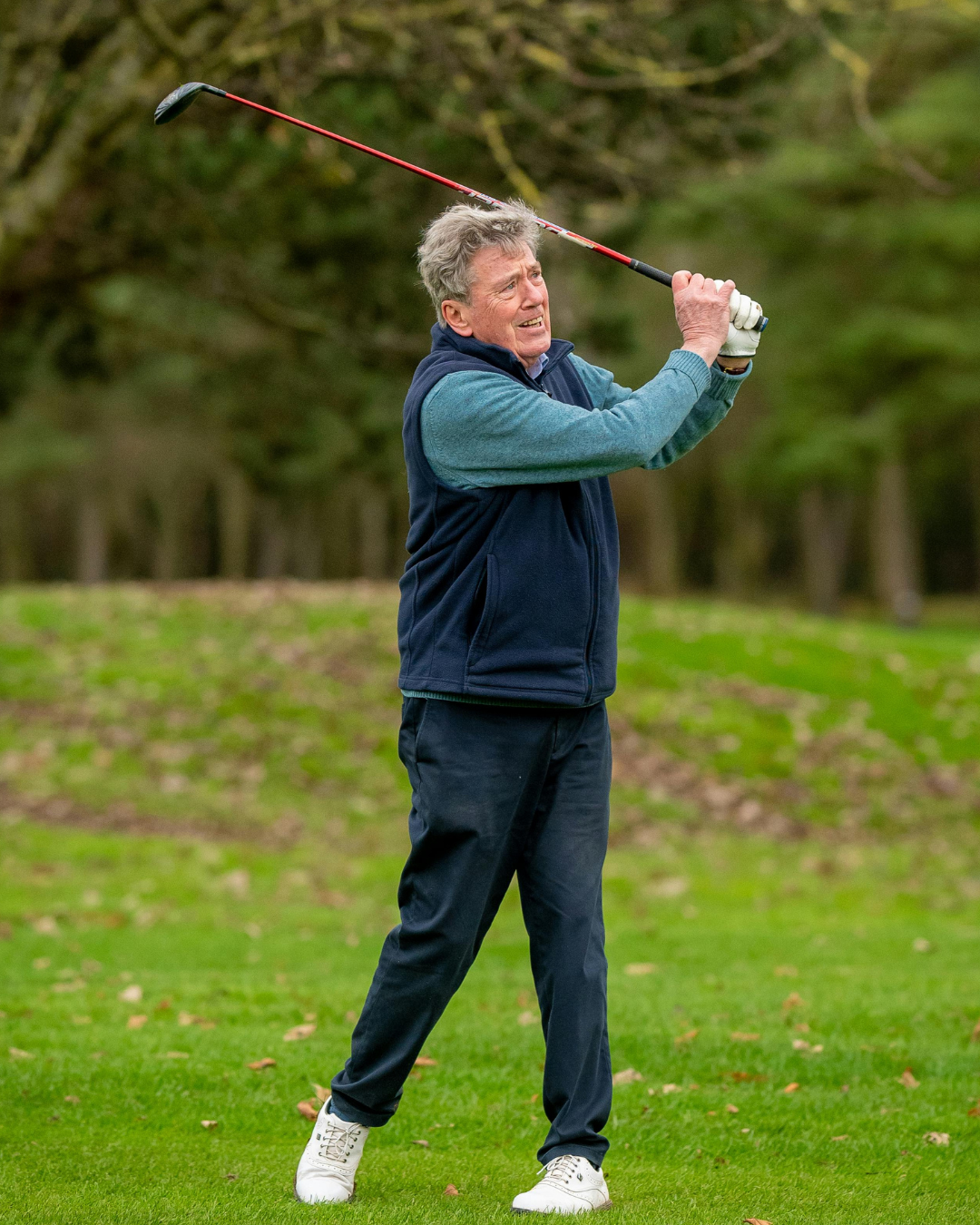 Photograph of an older man mid golf swing on a grassy course, weight shifted through the hips and legs, highlighting rotation and load through the hip and outer thigh that can stress the IT band over time.