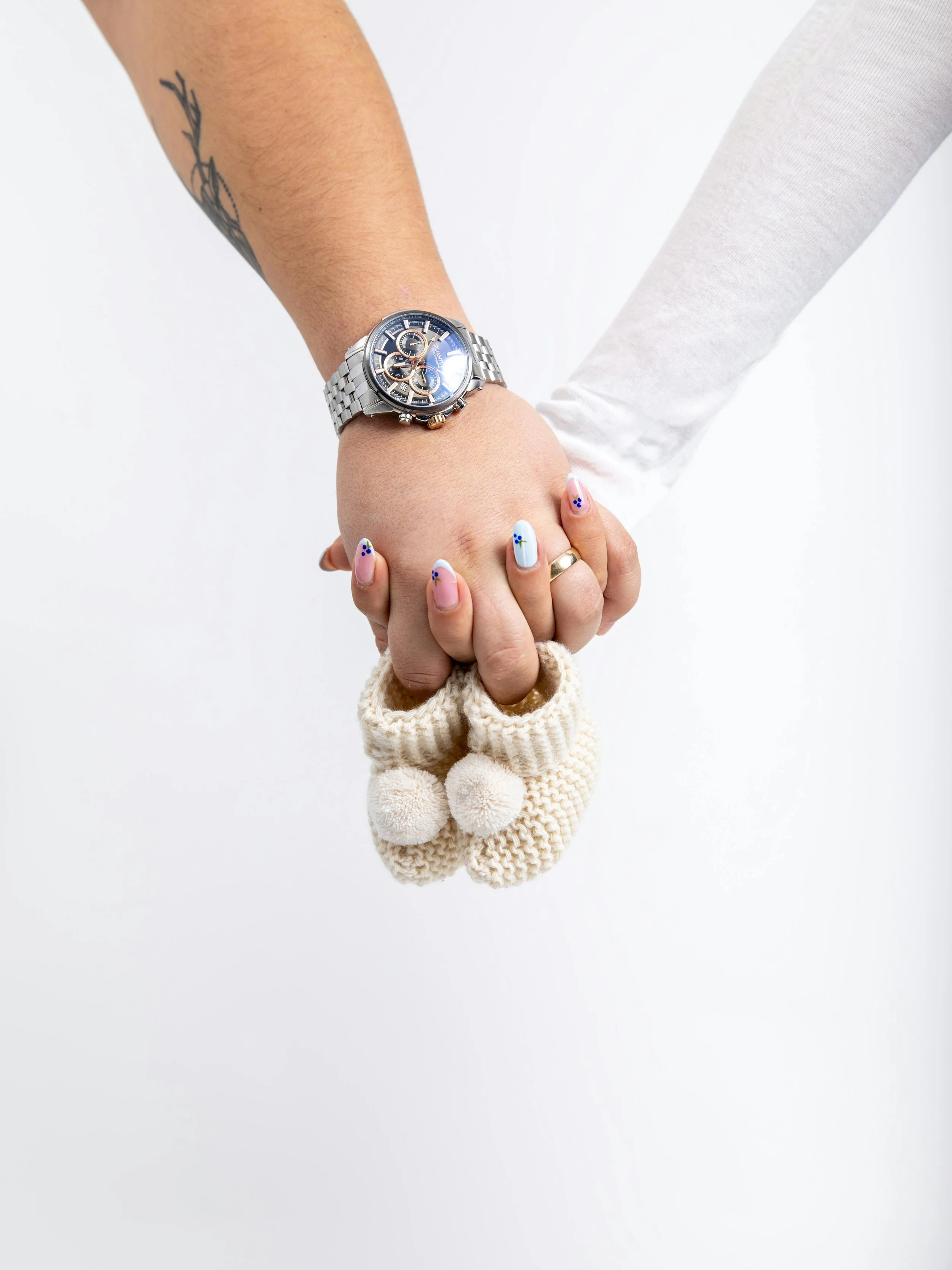 A couple holding hands together with a pair of tiny knit baby booties, representing first trimester support and early pregnancy acupuncture at South Shore Acupuncture and Wellness, Rockland MA.