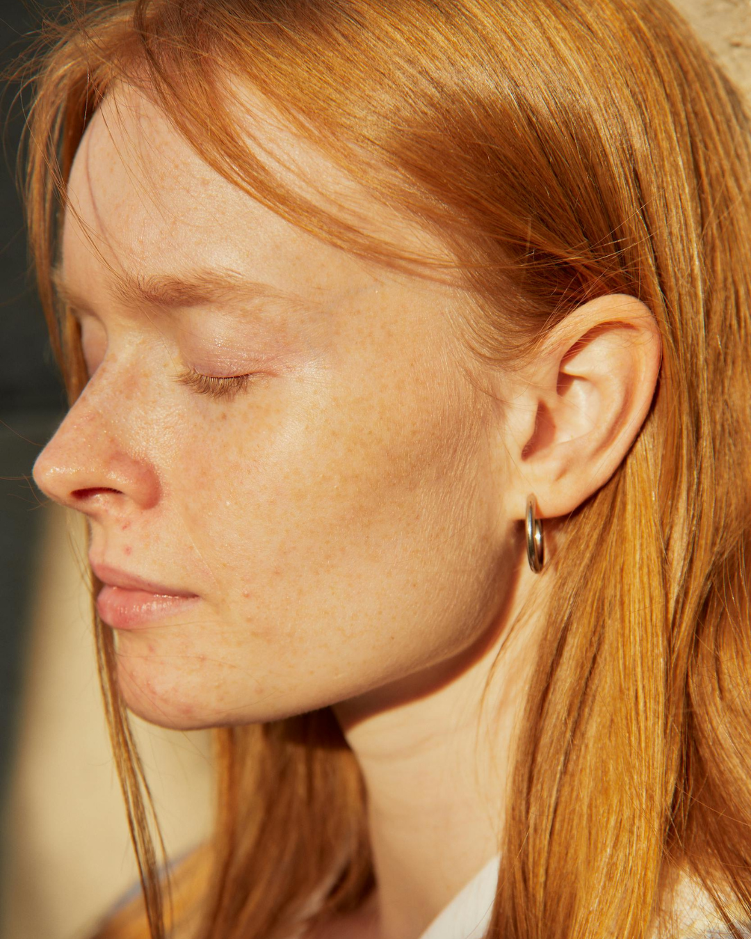 Close up profile photograph of a woman with her eyes closed, warm light highlighting the jawline, cheek, and ear, suggesting stillness and subtle tension in the jaw and face.