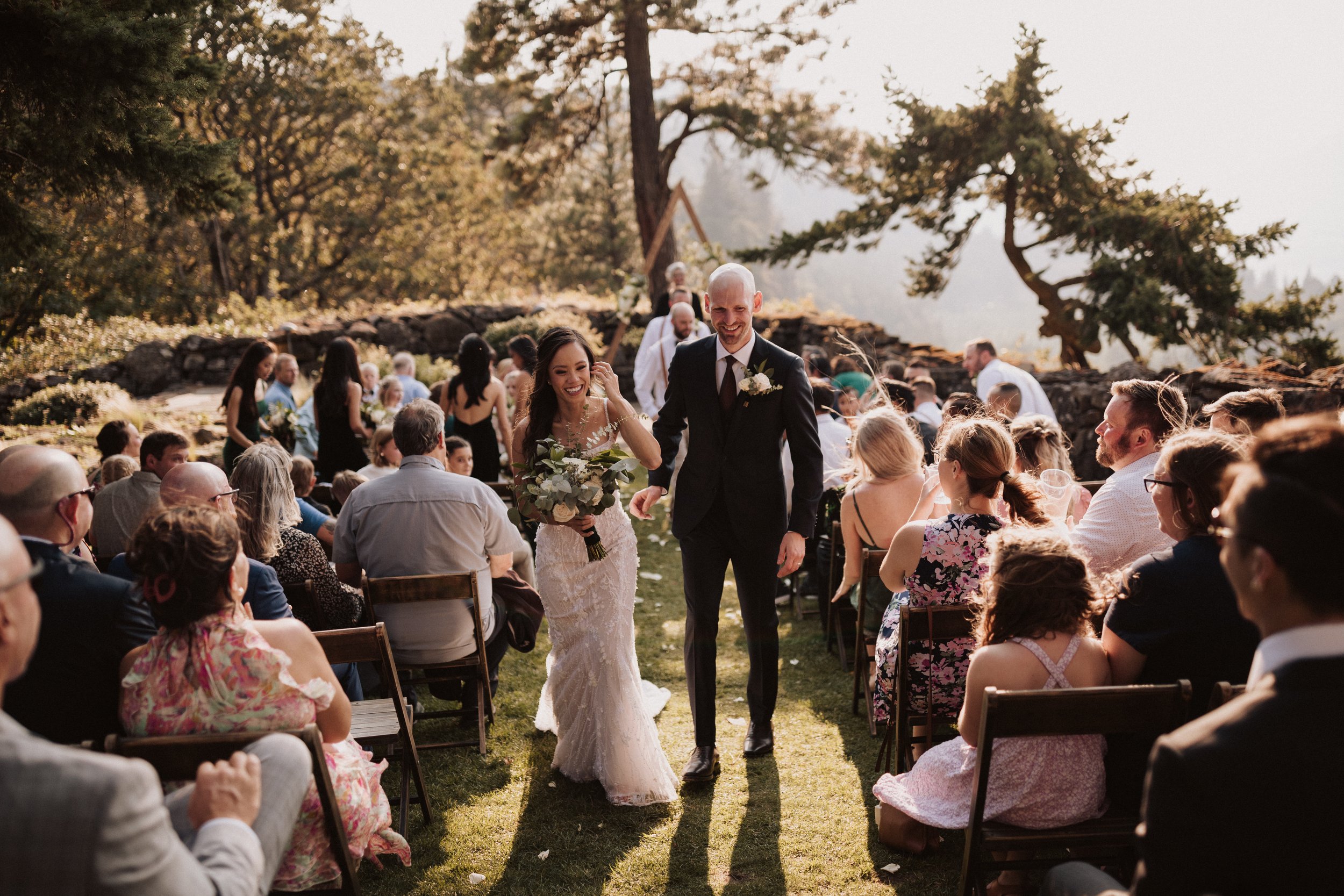 Wedding ceremony outdoors with a couple holding hands and exchanging vows, surrounded by floral arrangements and guests.