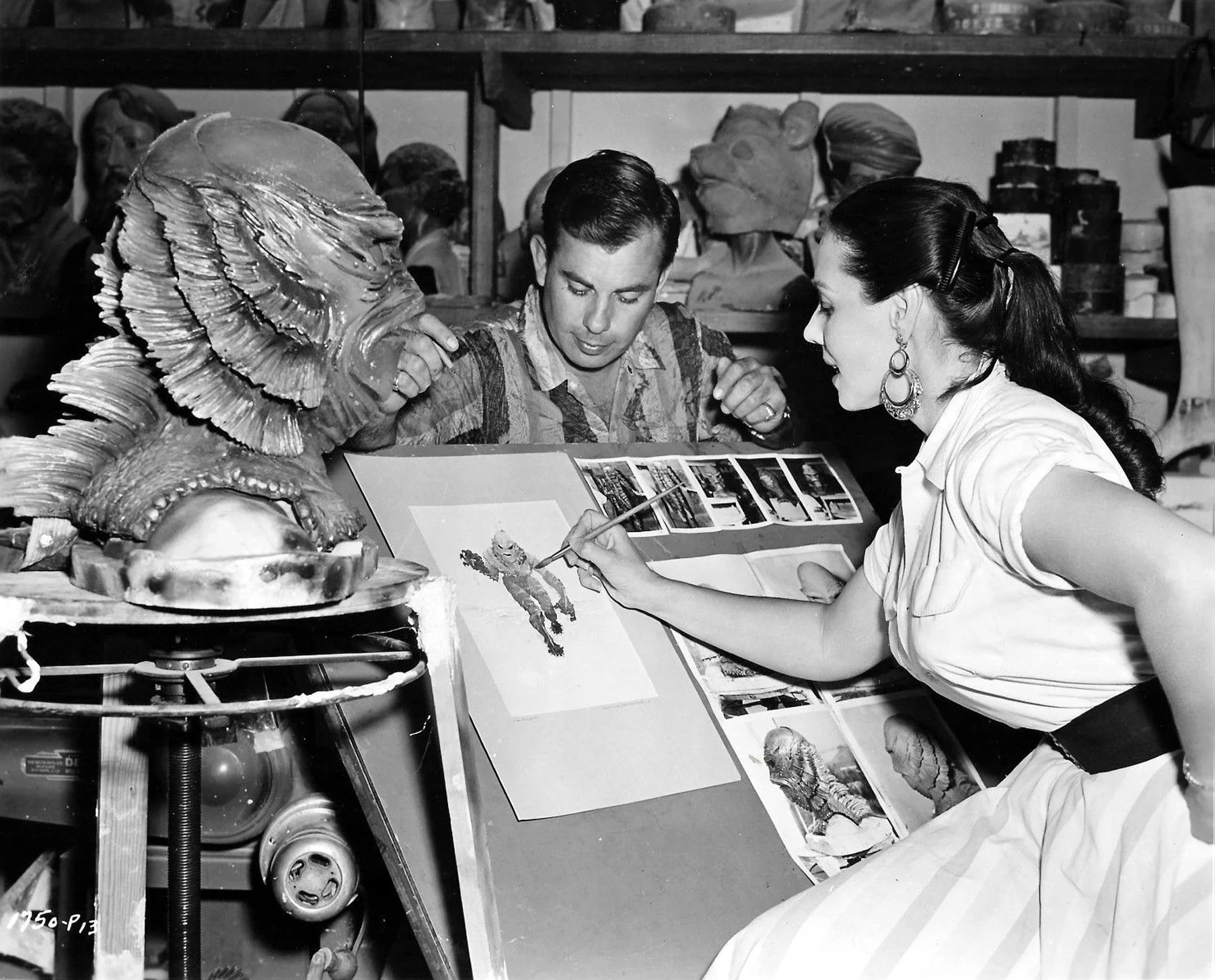 Milicent Patrick creating watercolor artwork of the Gill Man, with jealous asshole Bud Westmore “supervising.” | Source: Milicent Patrick Facebook Fanpage