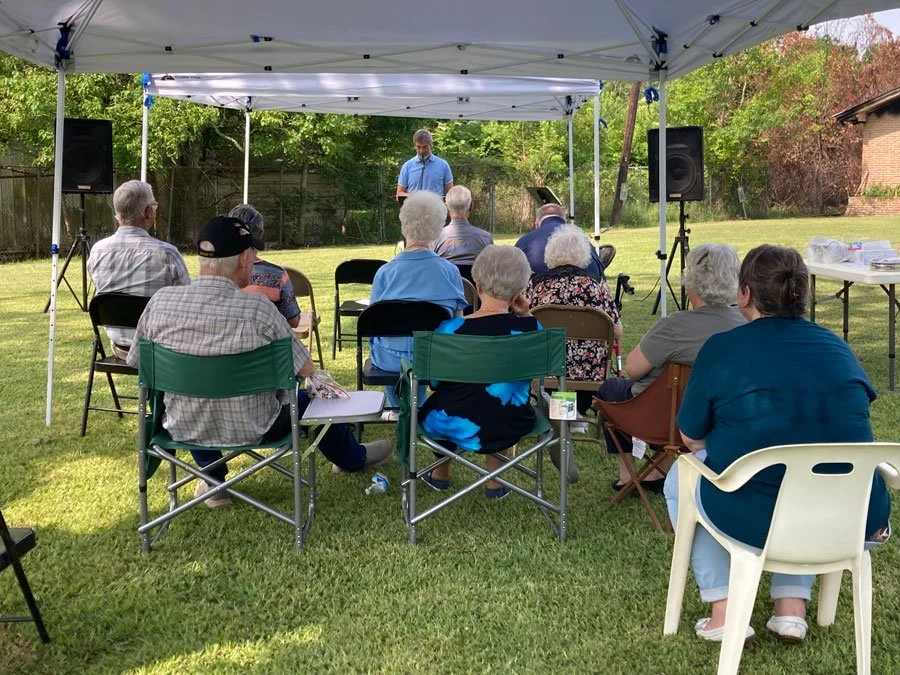 congregation under canopies on outside lawn listening to preacher