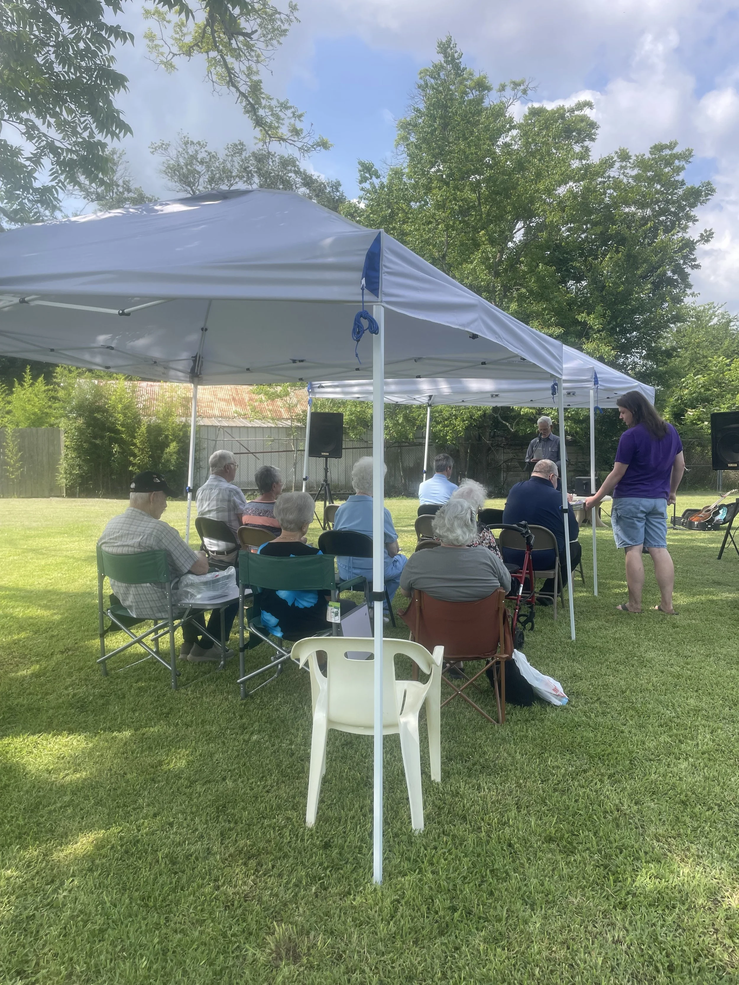 congregation under canopies on outside lawn listening to speaker, man serving communion