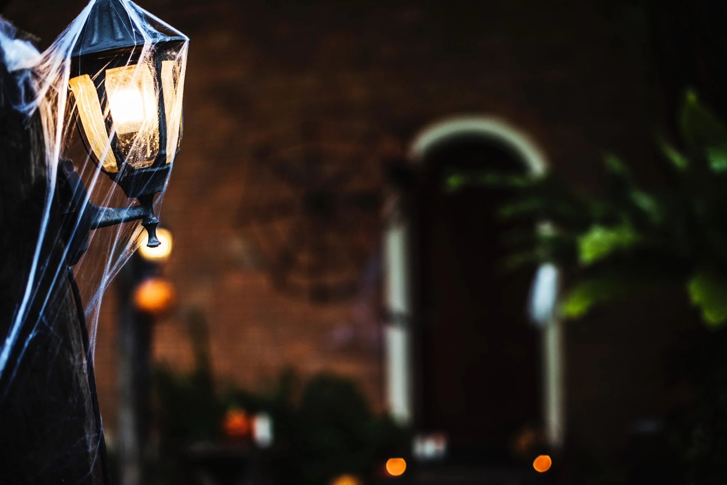 A lit exterior candelabra covered in cobwebs with a spooky house entrance in the background.